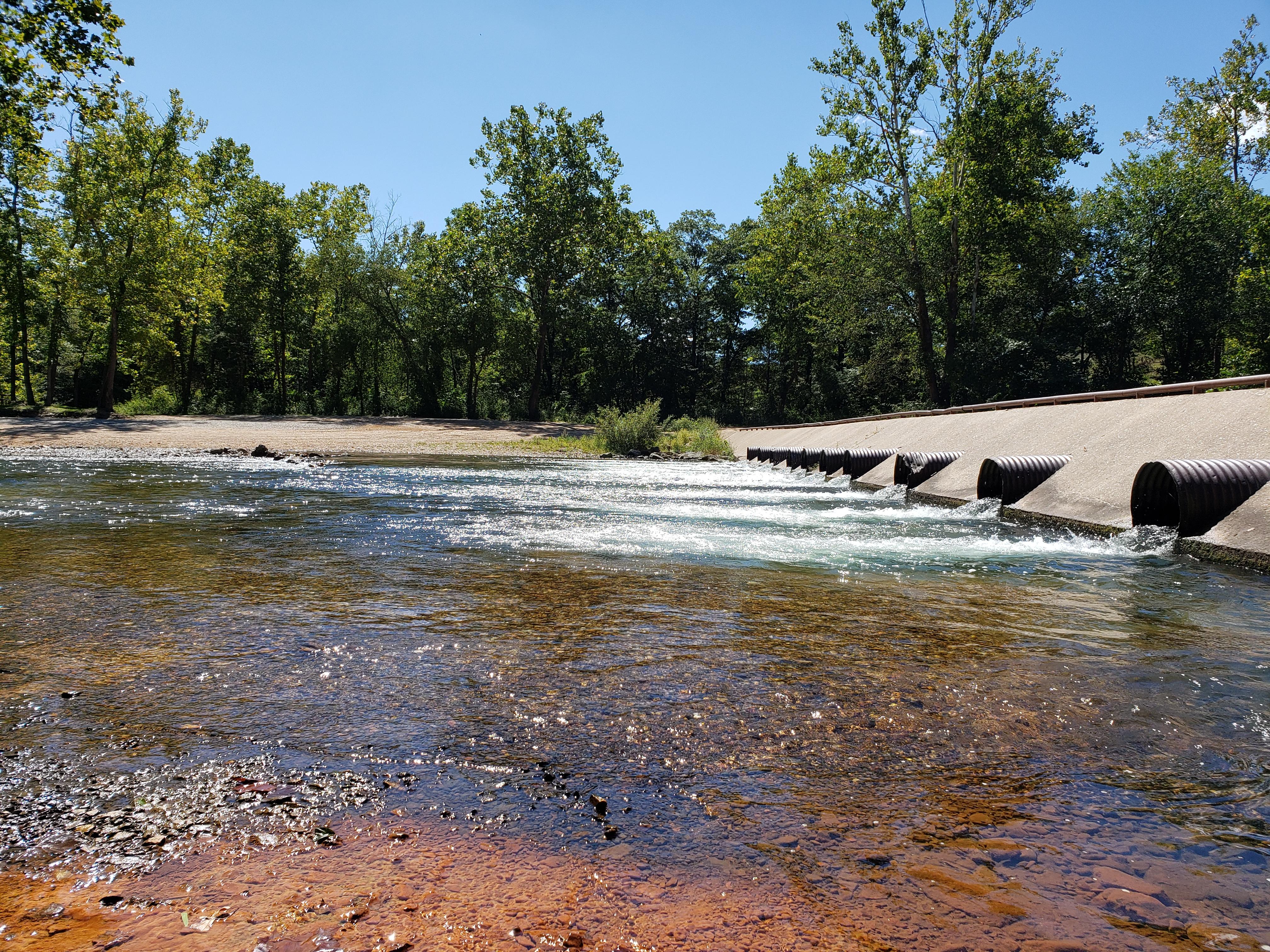 A concrete culvert with water rushing through large pipes.