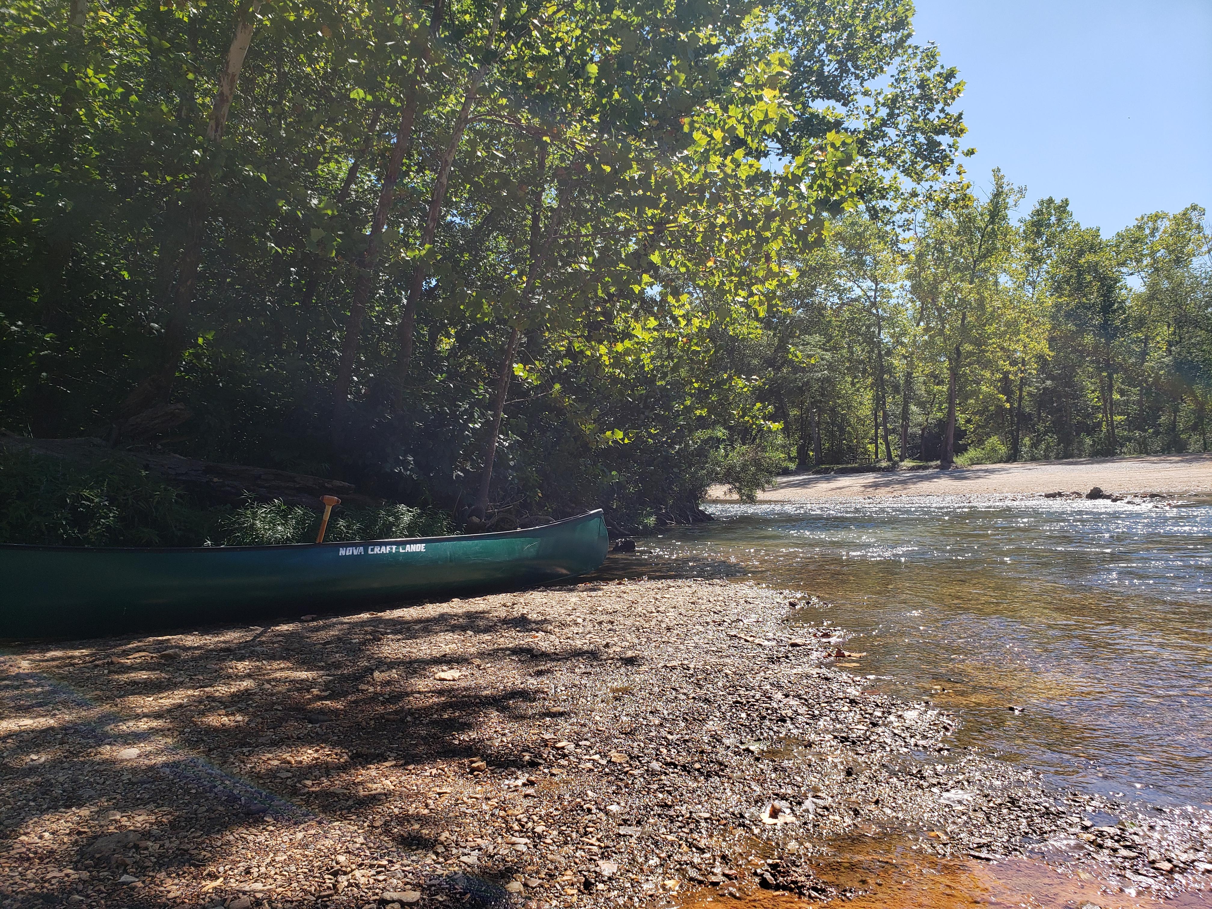 A canoe sits on a shaded gravel bar.