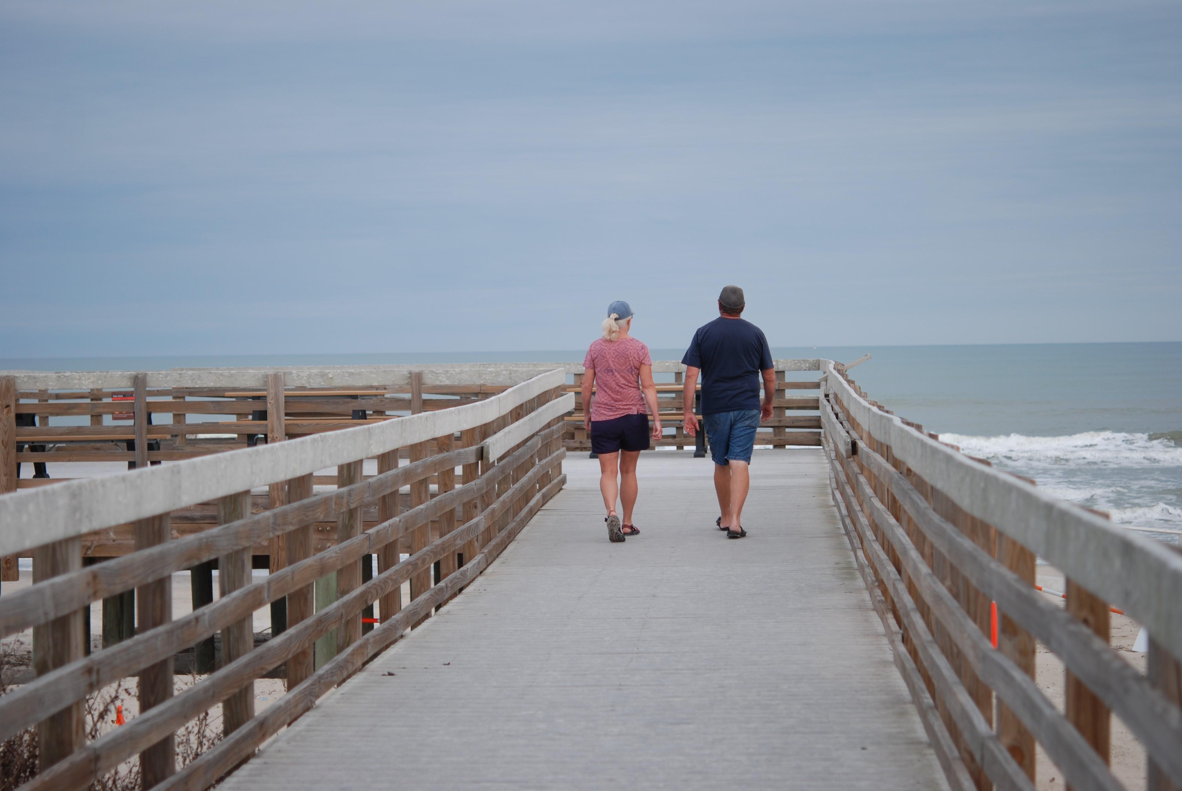 Two people walk towards the beach on the boardwalk.