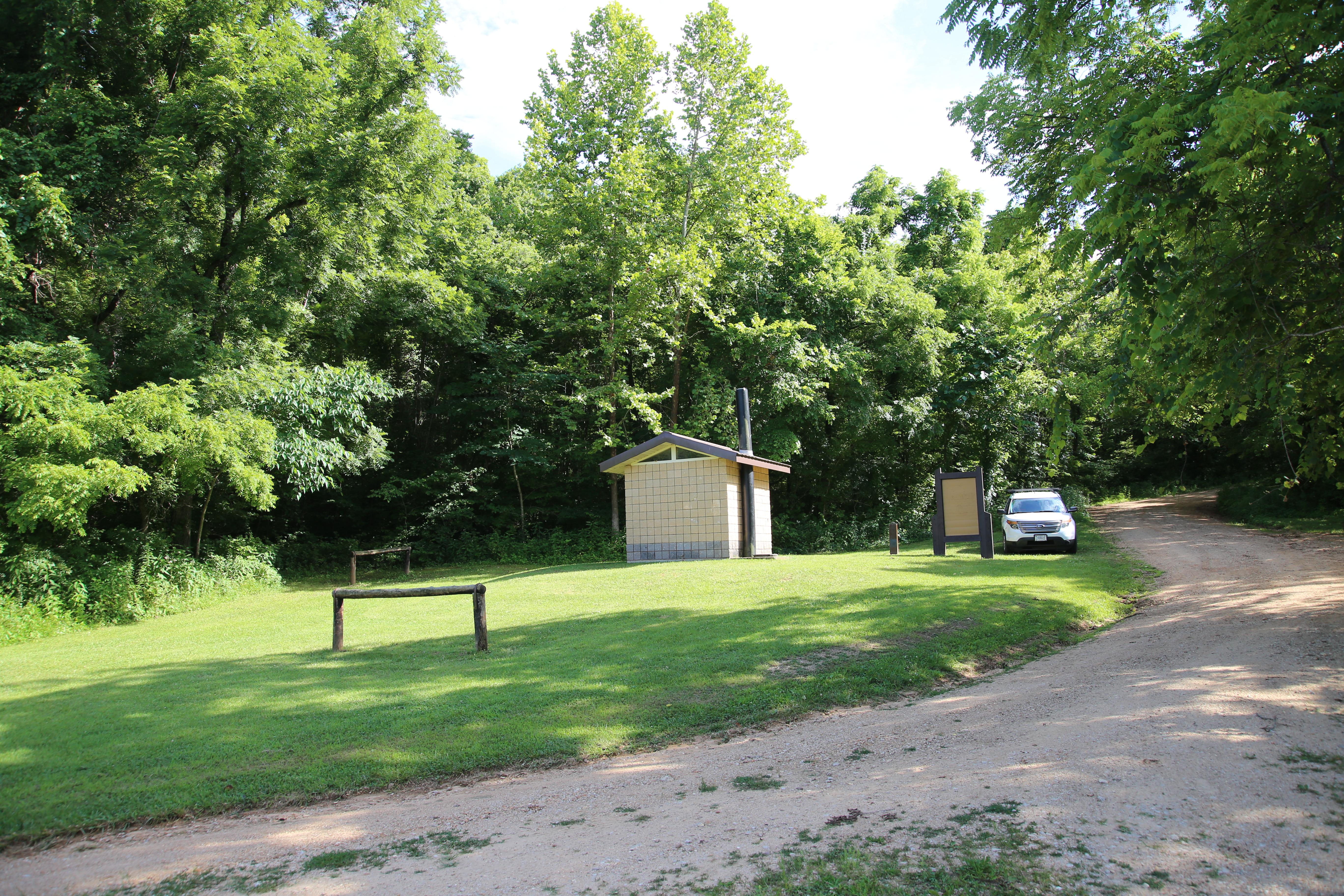 A tiled vault toilet building along a gravel road.