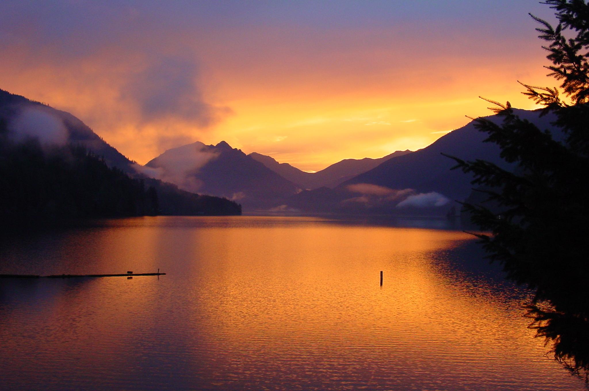 A lake surrounded by mountains reflects a brilliant orange sunrise.