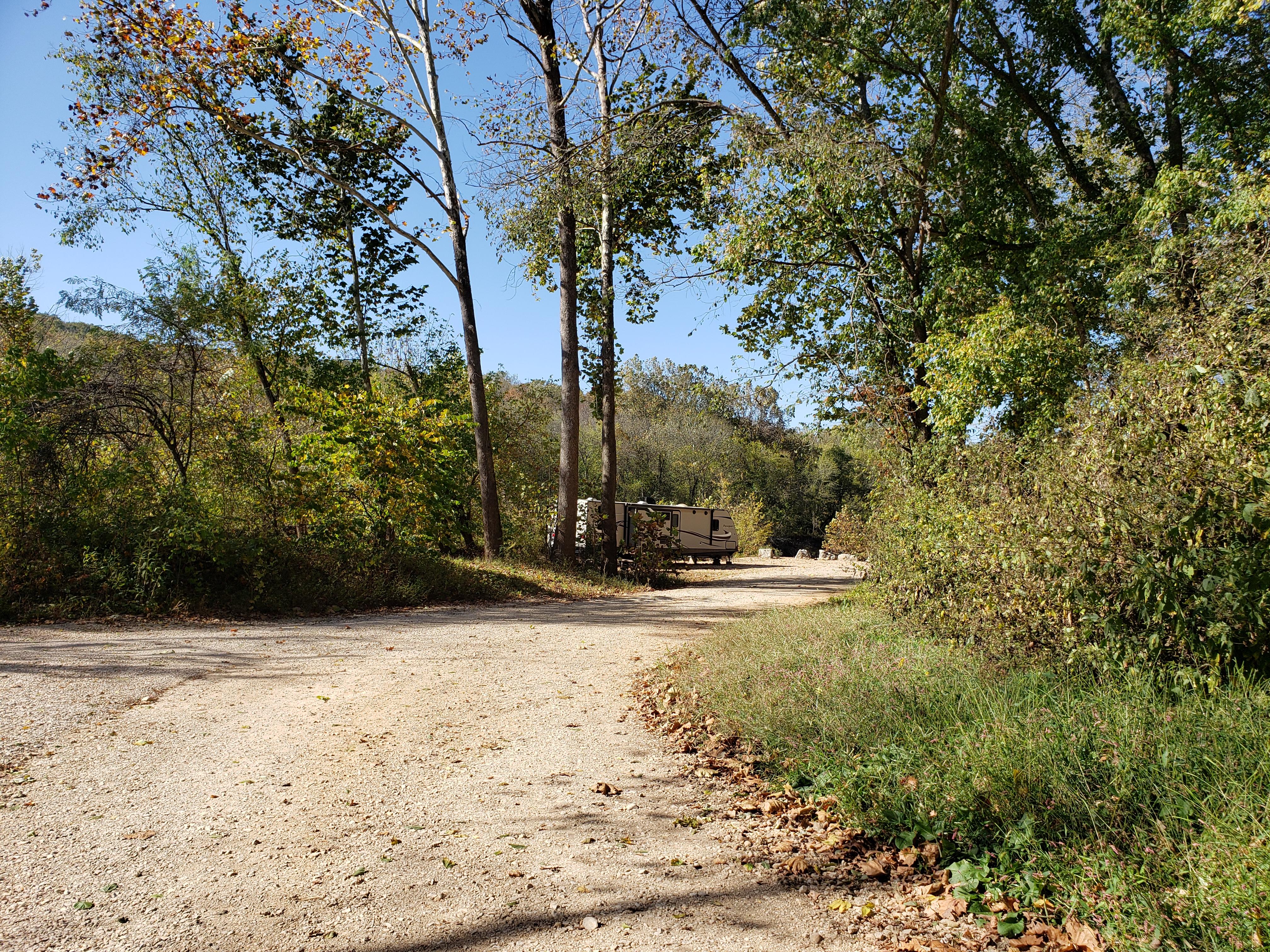 A gravel road passes a sunny campsite with an RV.