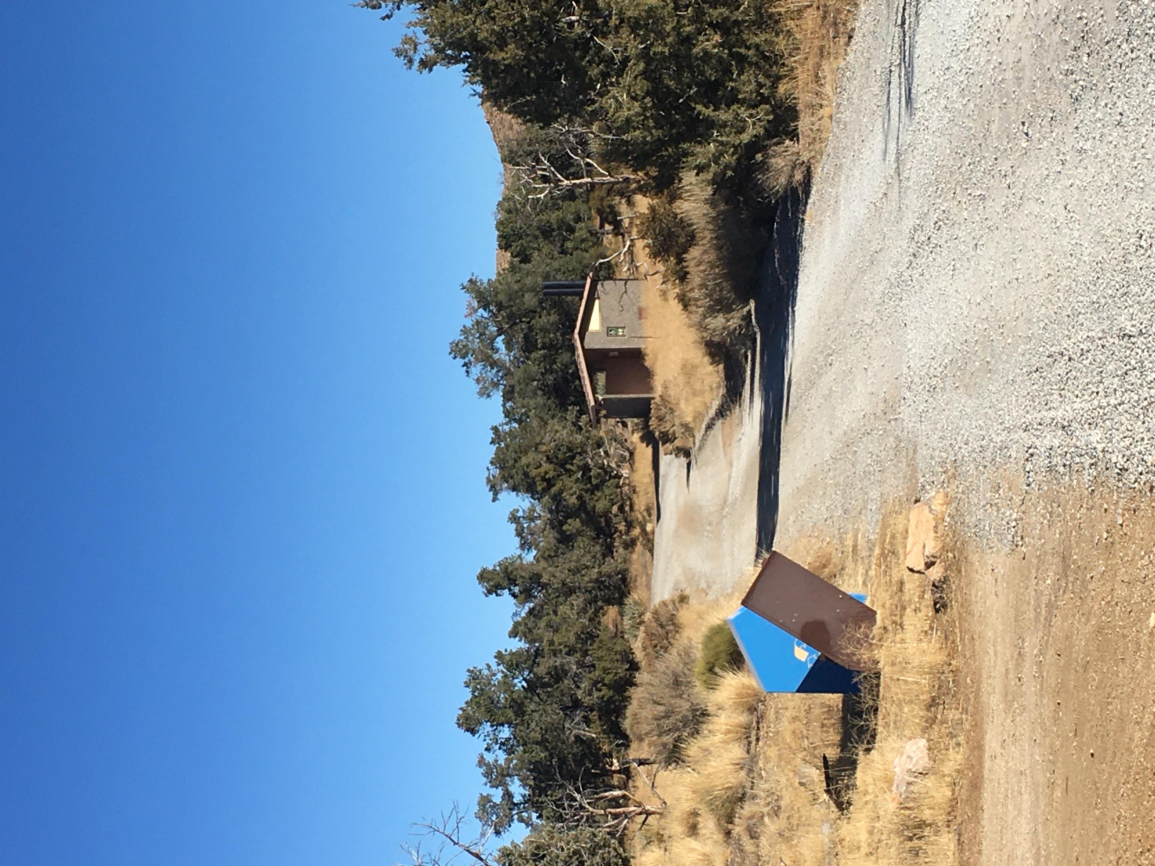 A campground road. Garbage and recycling containers and a bathroom building are also shown
