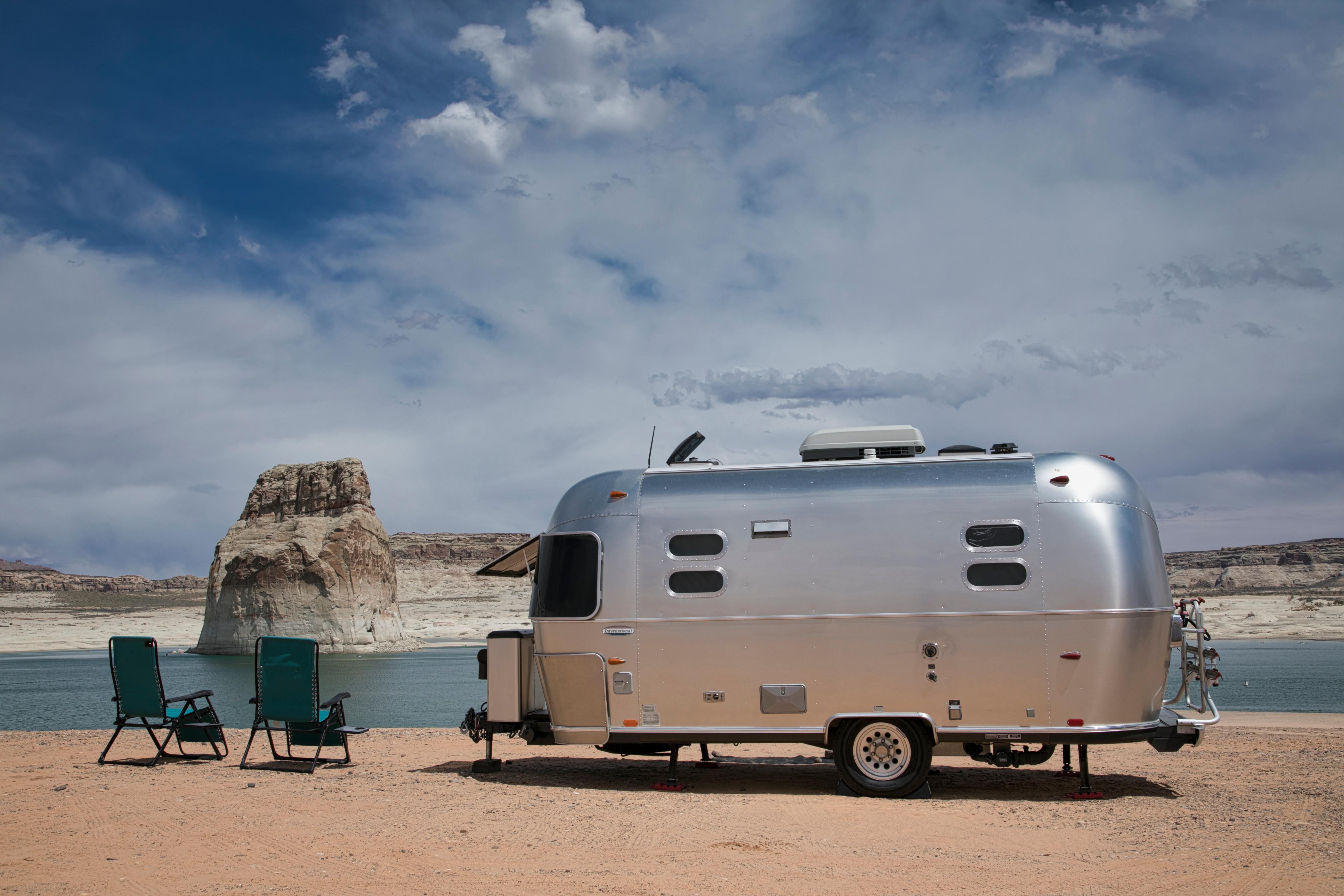 Airstream camper and beach chairs on beach next to lake and sandstone cliffs