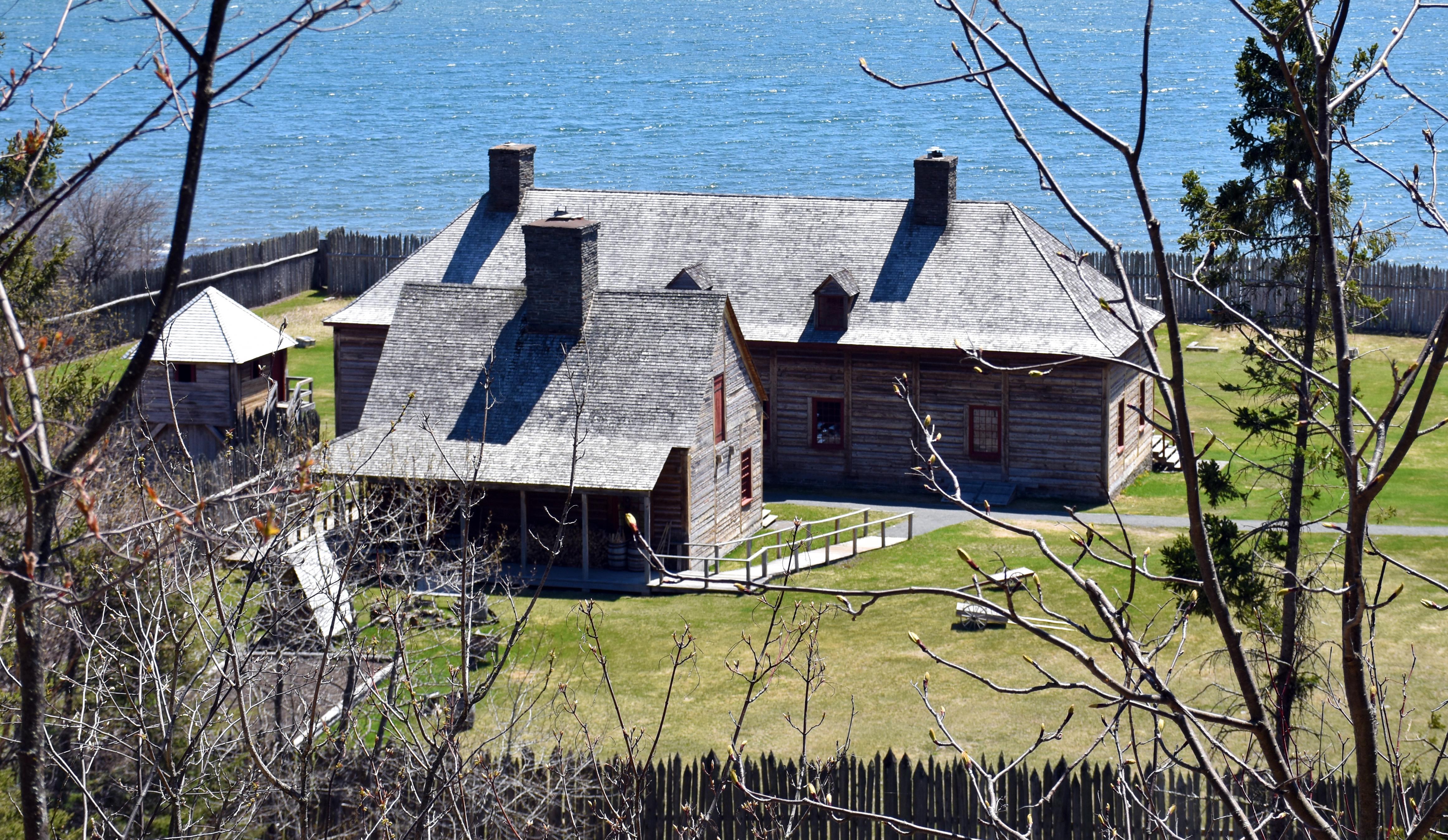 Historic wooden buildings on a bright green lawn in front of a lake.