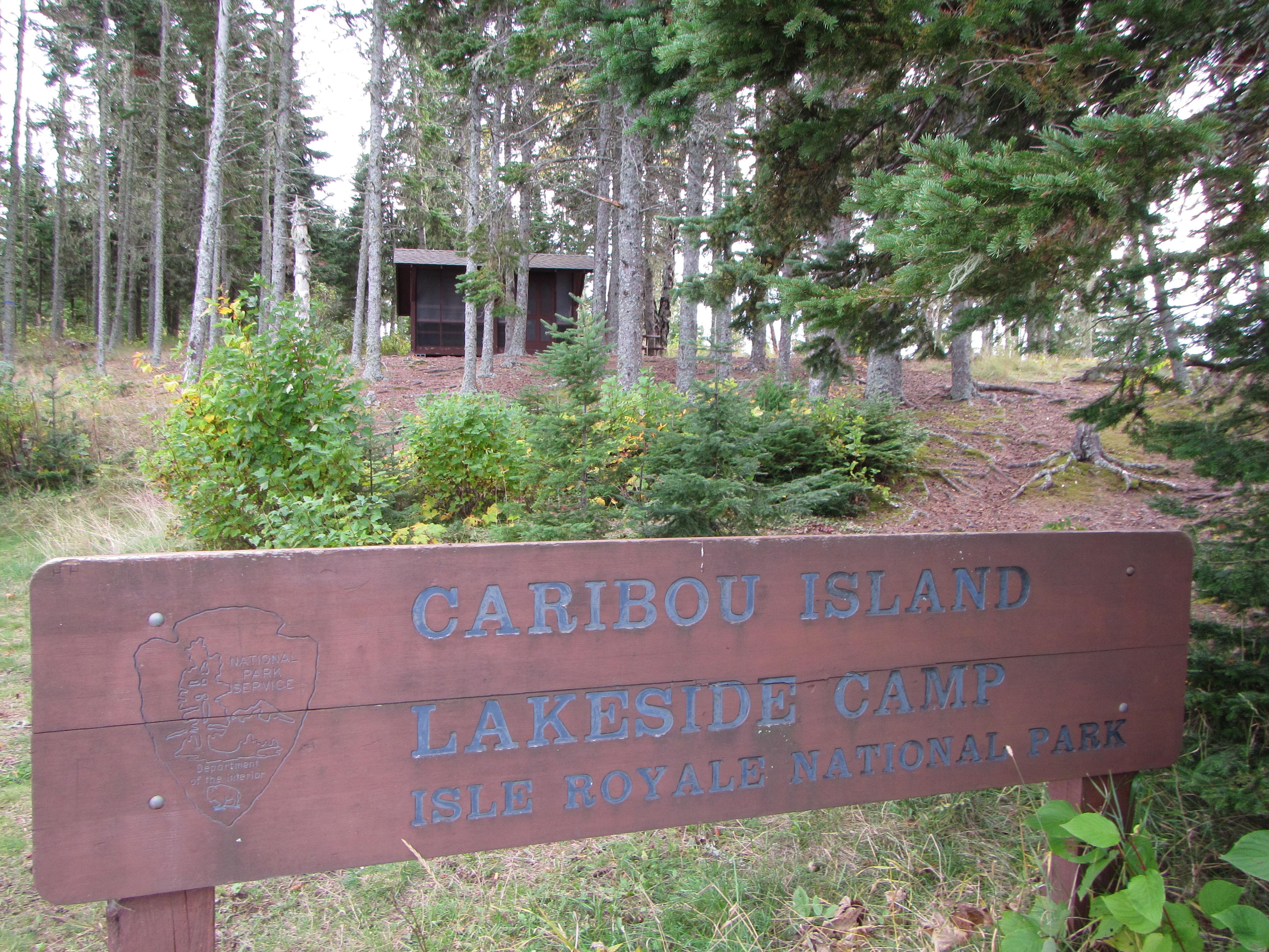 Caribou Island sign with shelter in the distance behind trees.