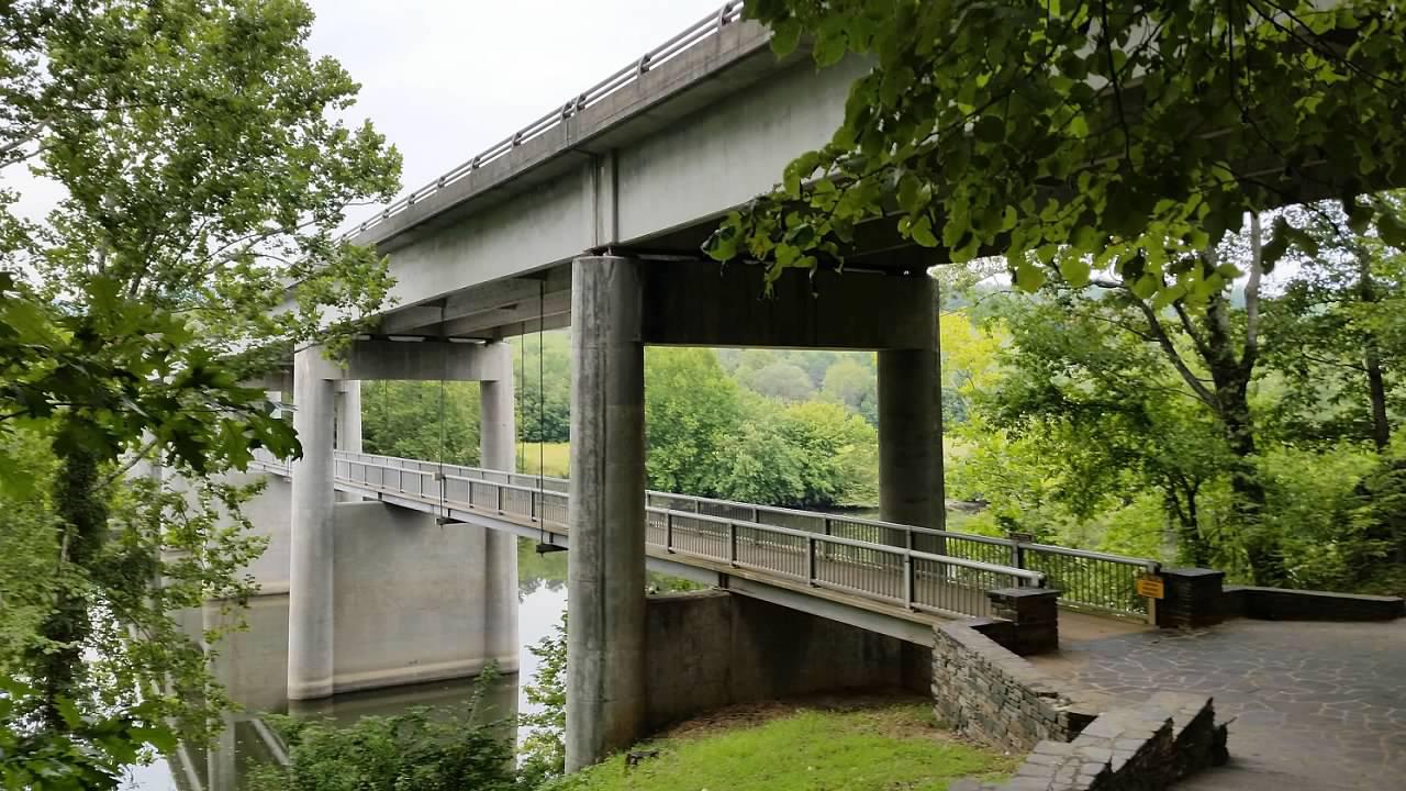 A concrete bridge with a pedestrian walkway underneath leads over a river.