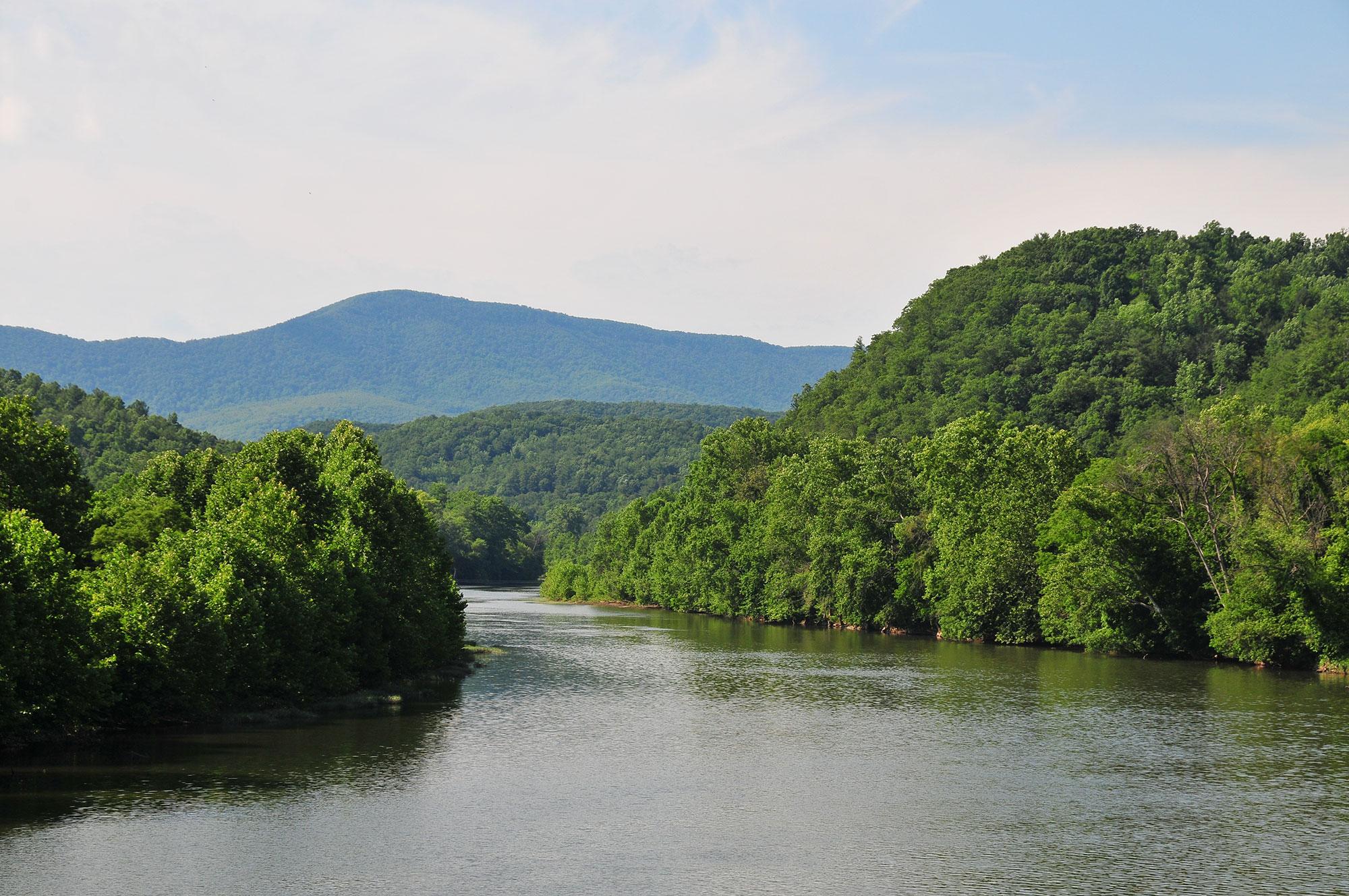 A broad river flows through forested hills, with a small mountain in the background