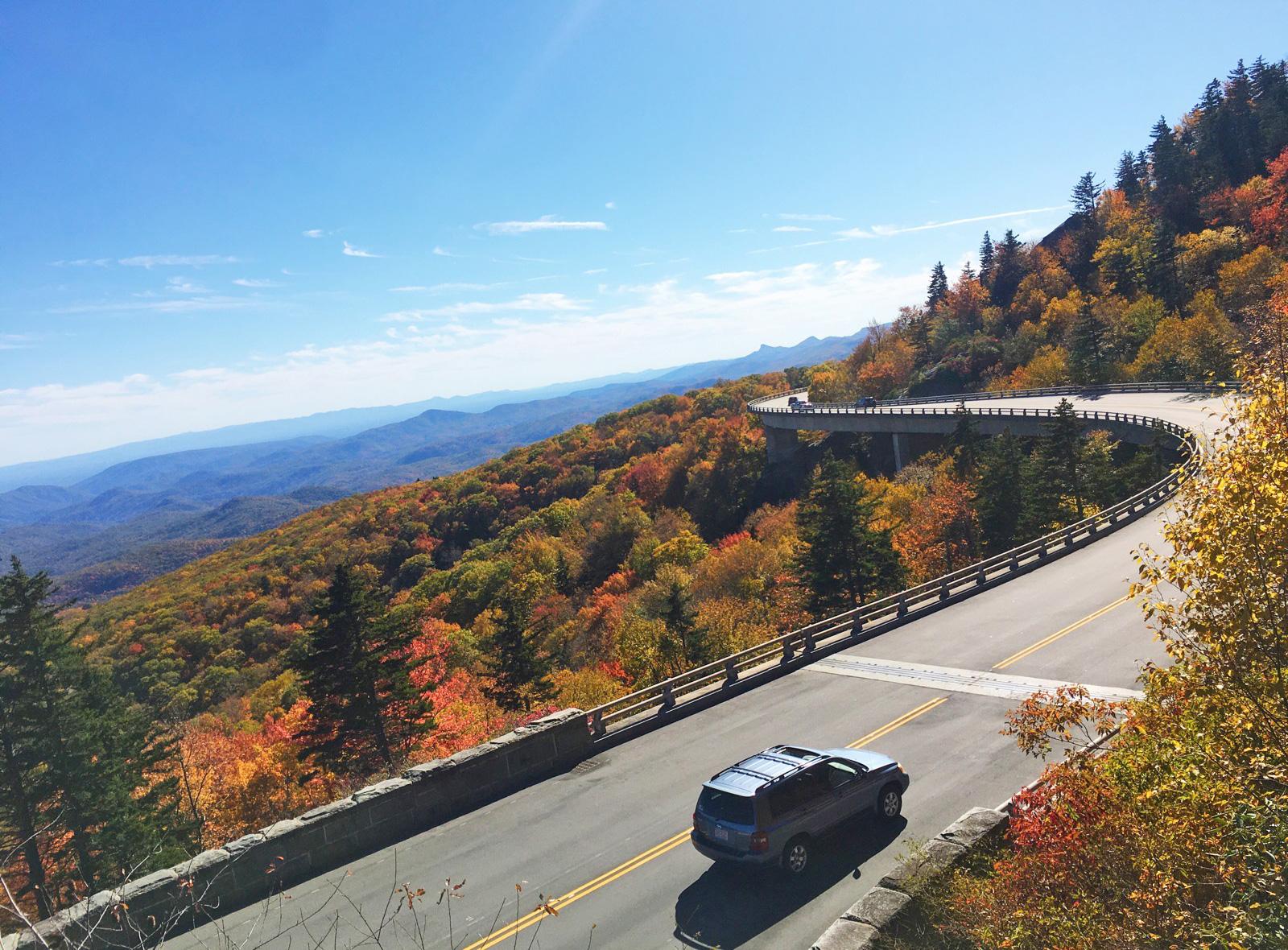 A car travels along a viaduct that hungs and curves along the side of a mountain.