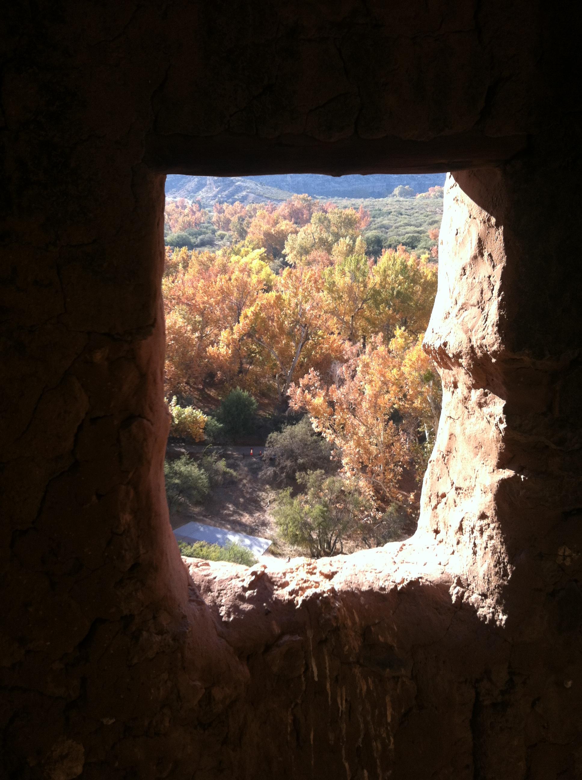 Sun shines on the window sill in a masonry wall; trees in fall color are seen outside the window.