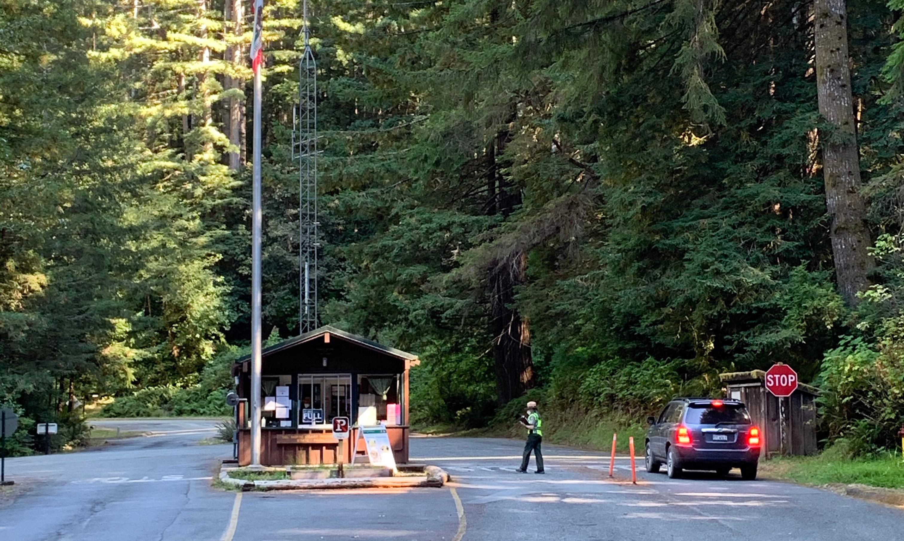 A small brown building bisects a road. A car is on the right.
