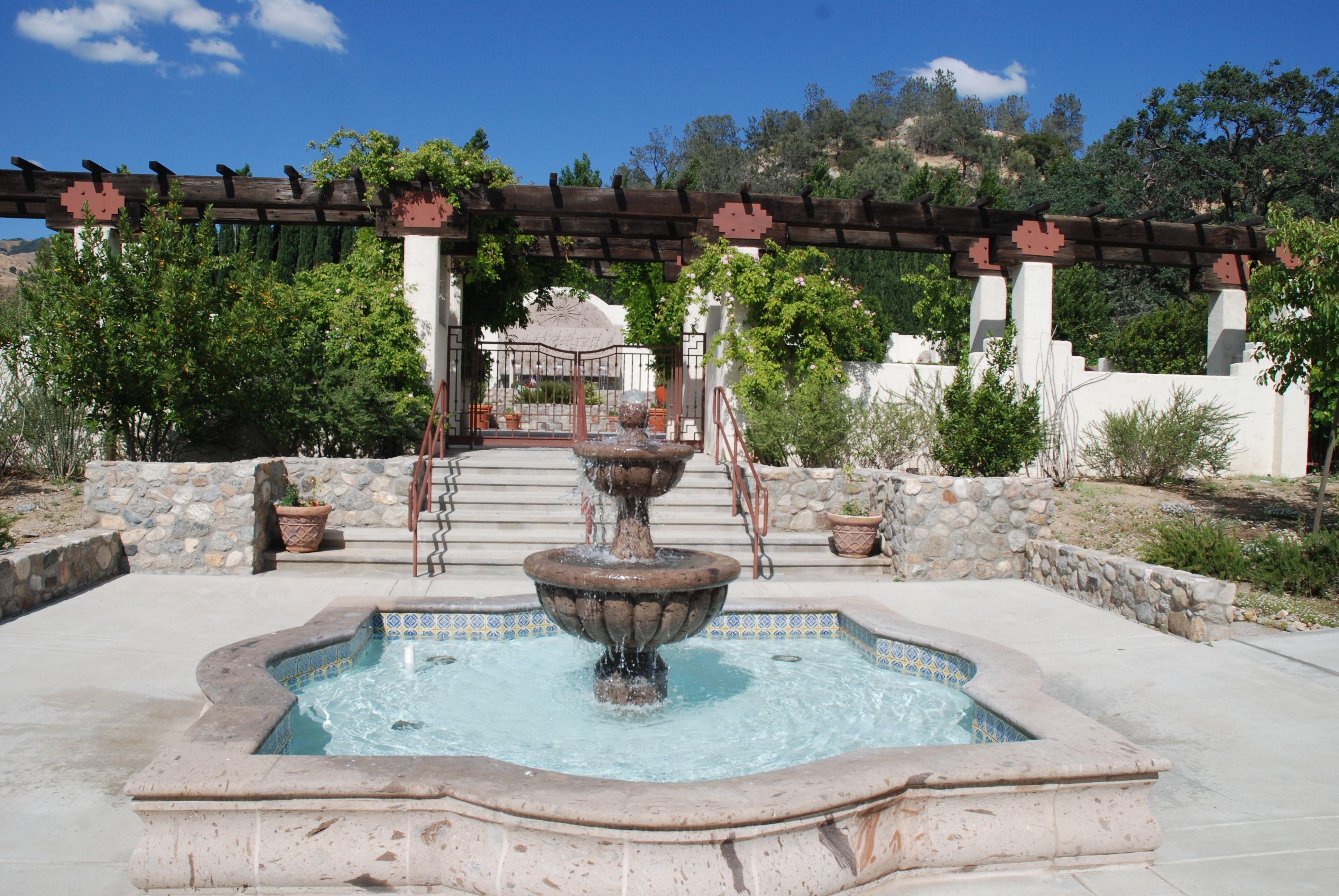 A two-tiered fountain in front of a set of stairs that go up to an arbor.