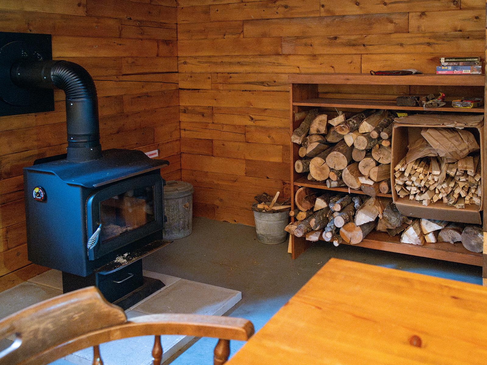 A black wood stove and dried kindling and logs ready for visitors inside the hut.