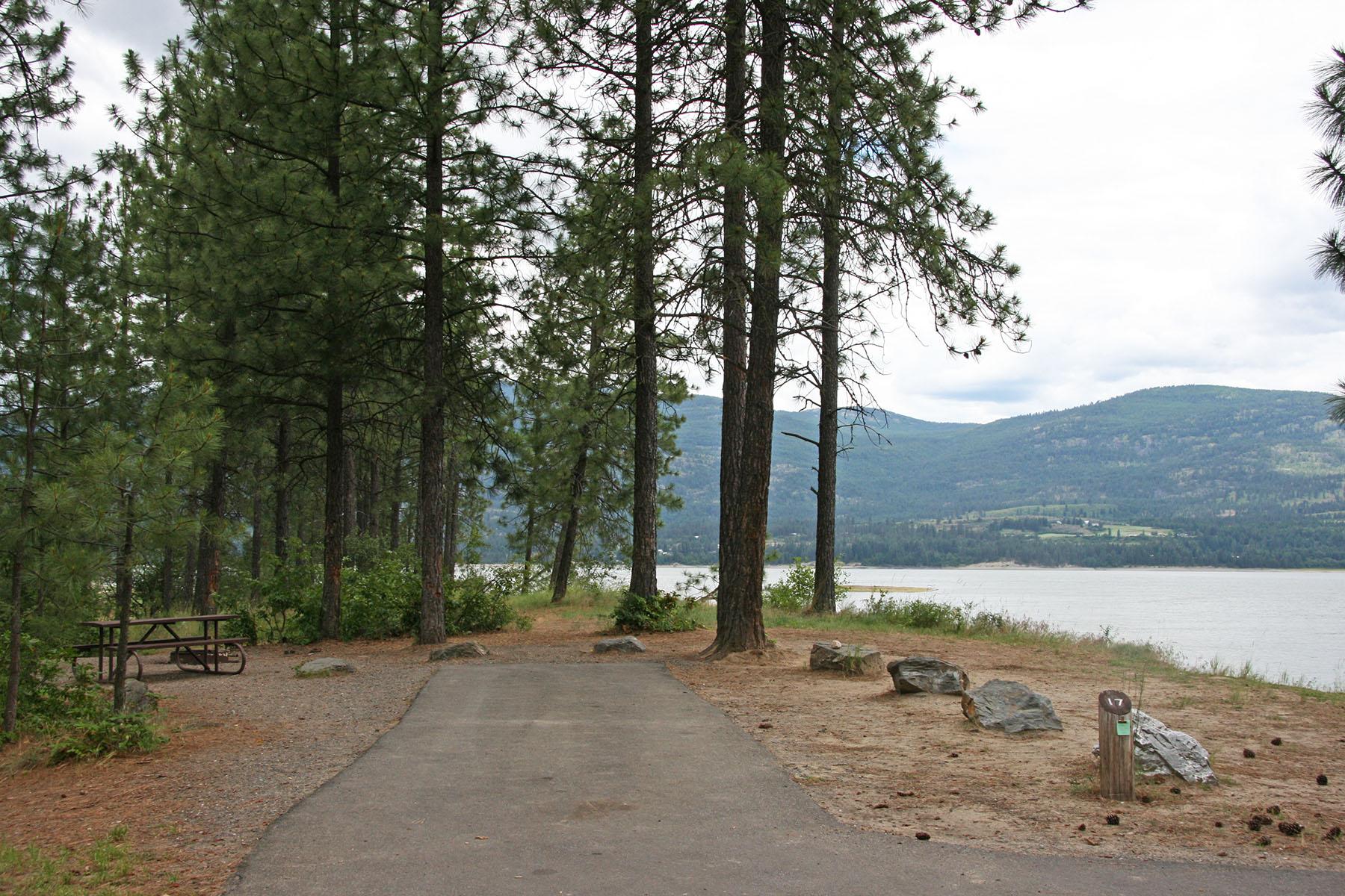 a paved parking spot next to the water, with picnic table and fire pit