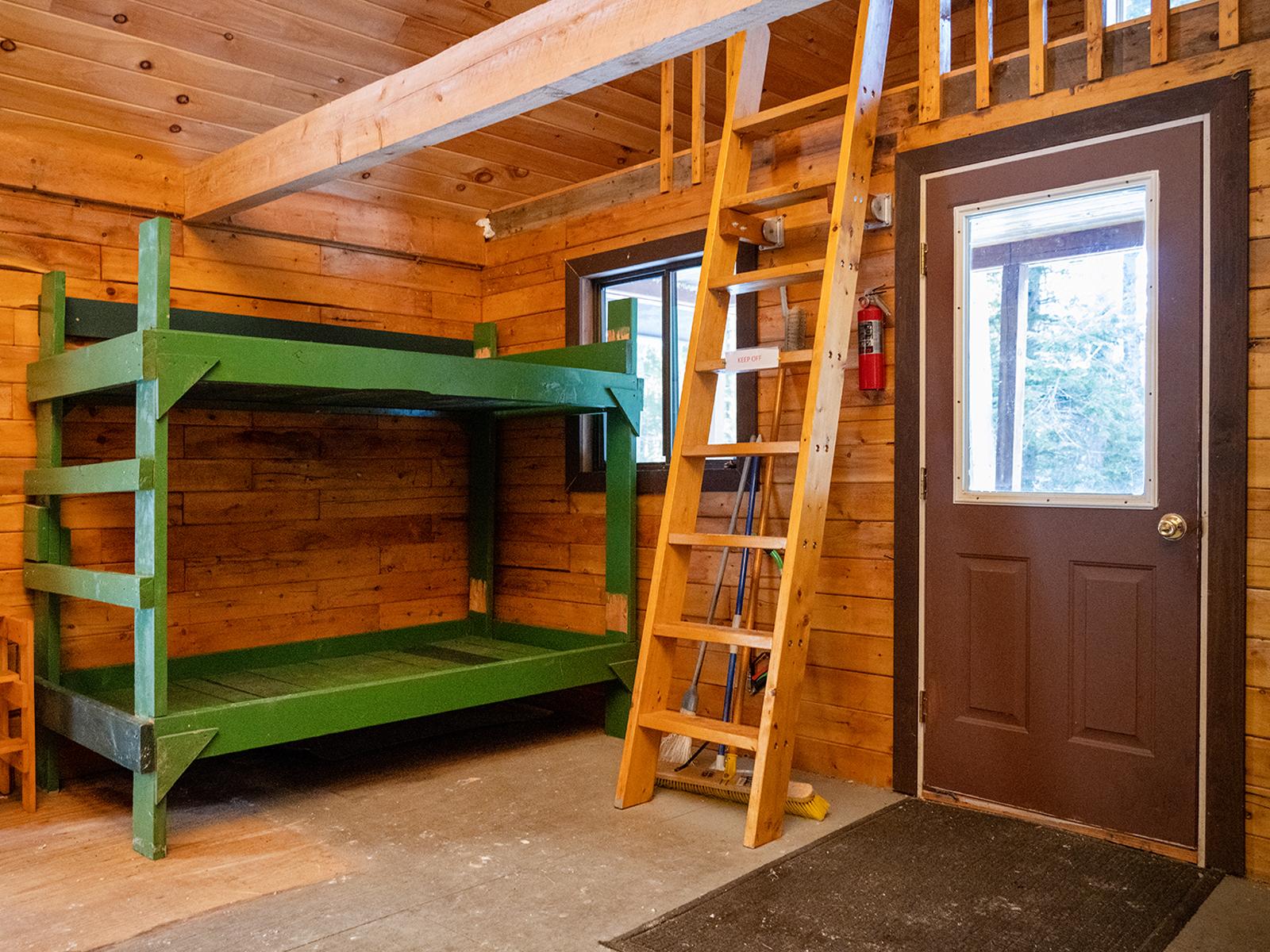 A green wooden bunk bed next to wooden ladder and door. The ladder has a keep off sign.