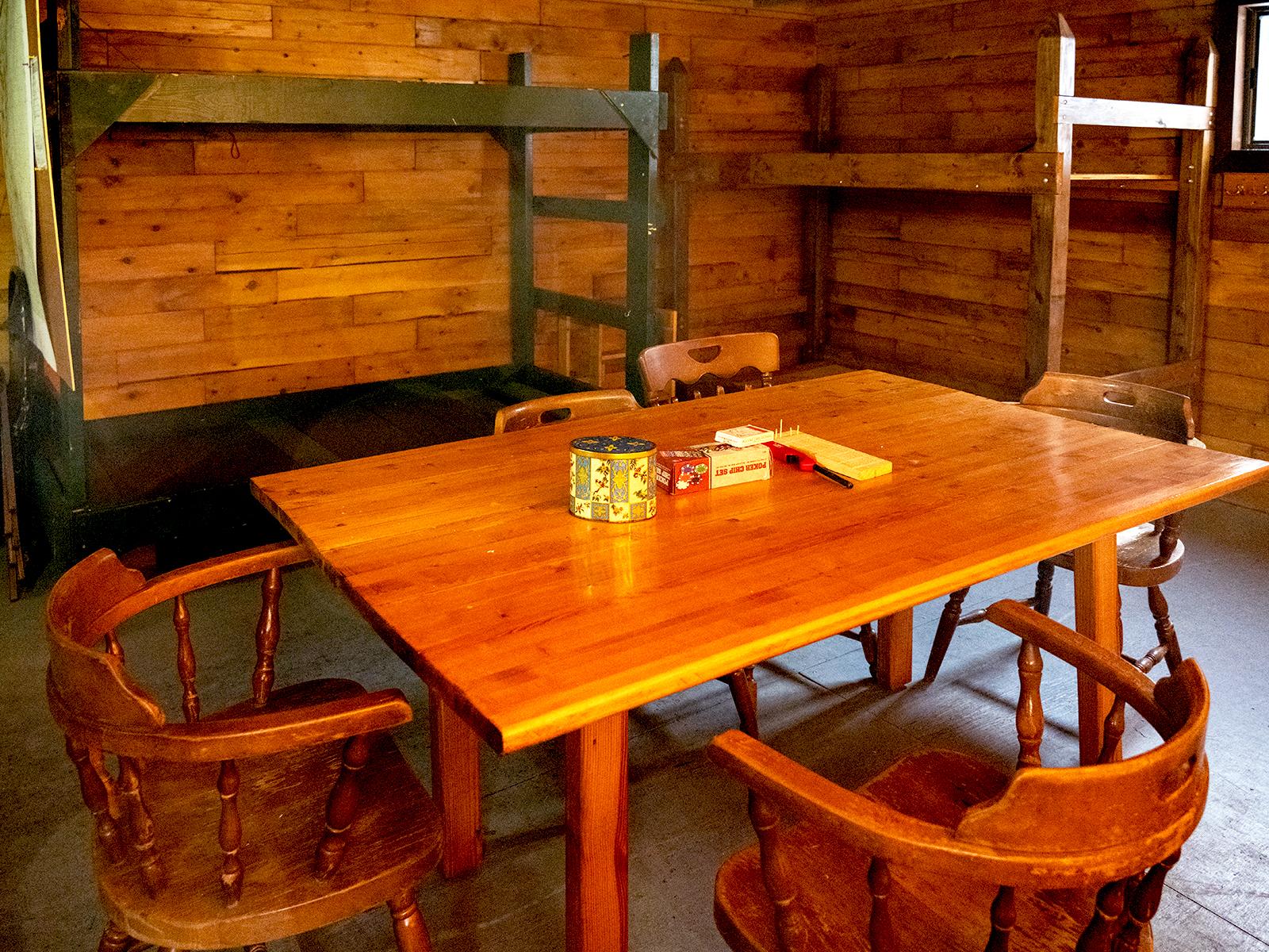 A wooden dining table is in the foreground with two wooden bucks against the wall in the background.