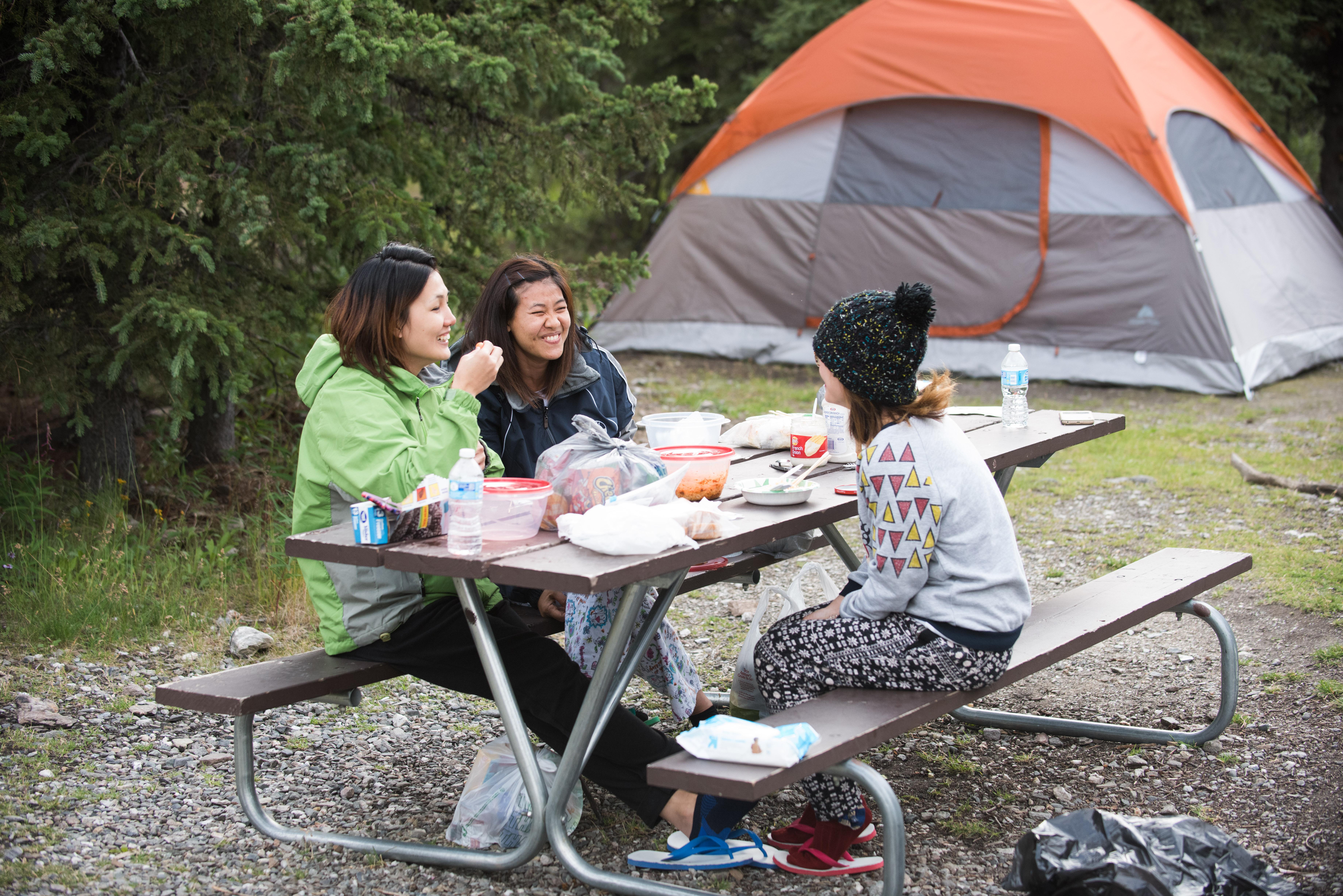 three women at a picnic table near a tent