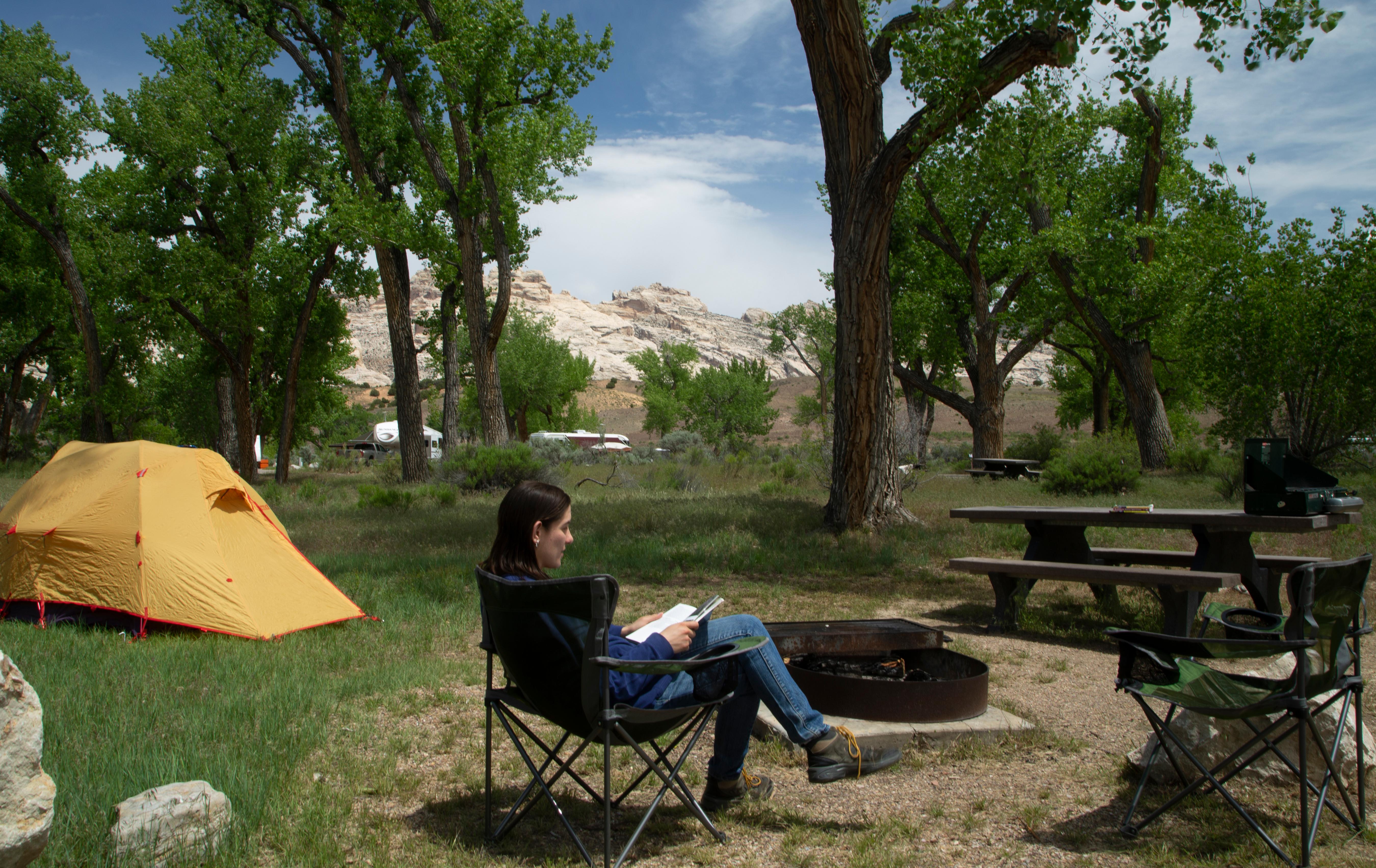 A woman reads a book in a chair in front of a yellow tent
