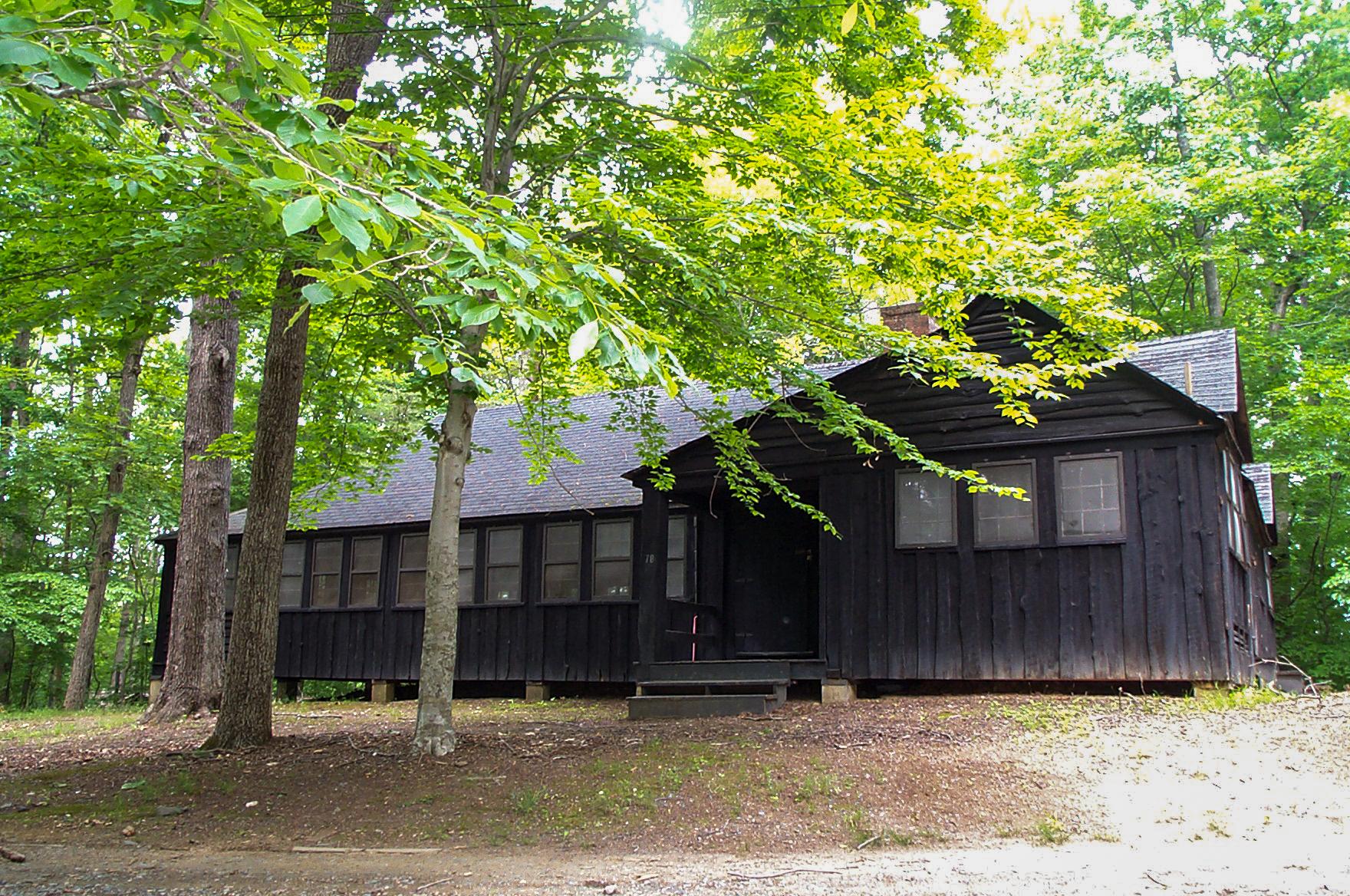 A  dark brown wooden building with a small front porch is among green trees