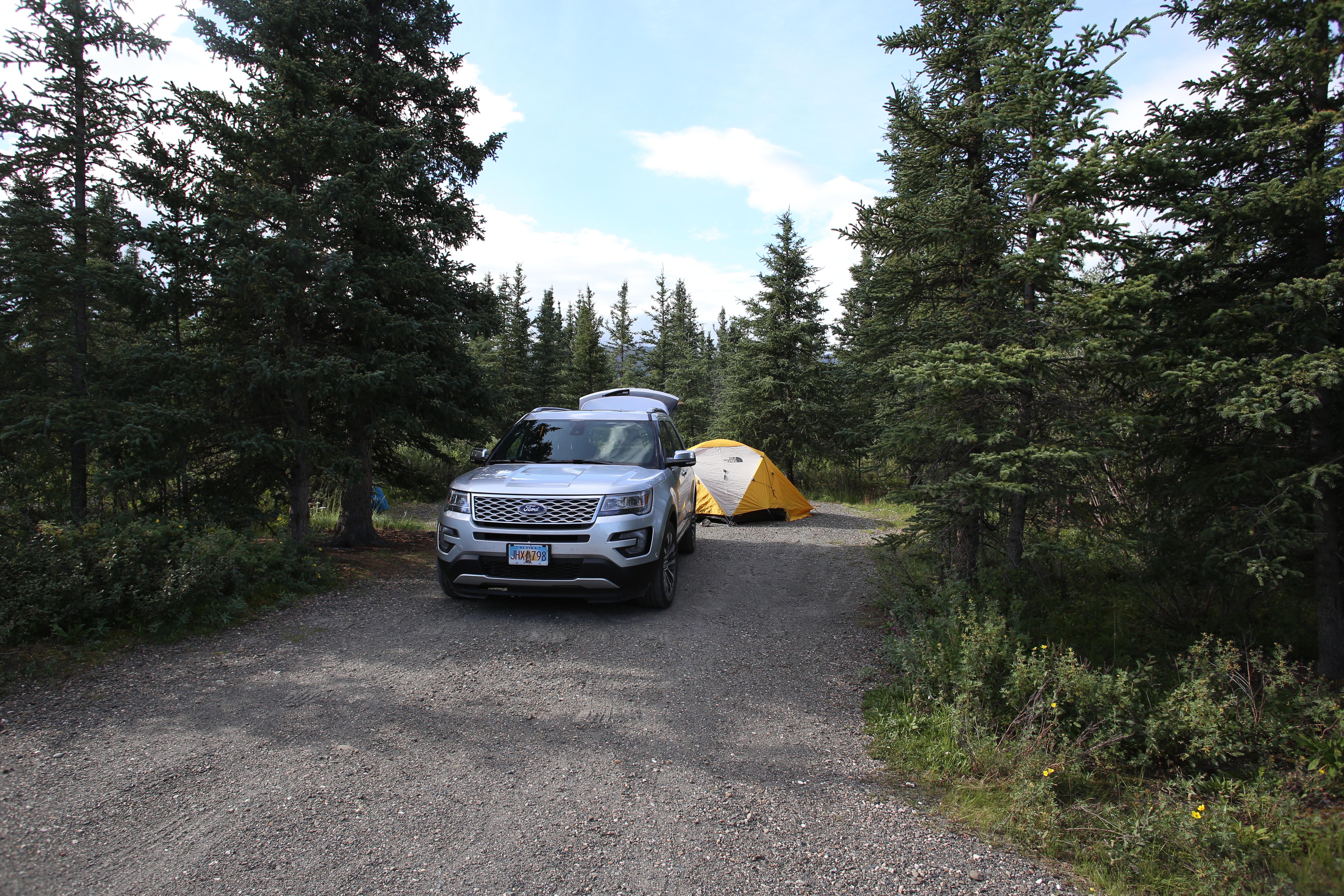 an SUV parked in a forest with a tent behind it