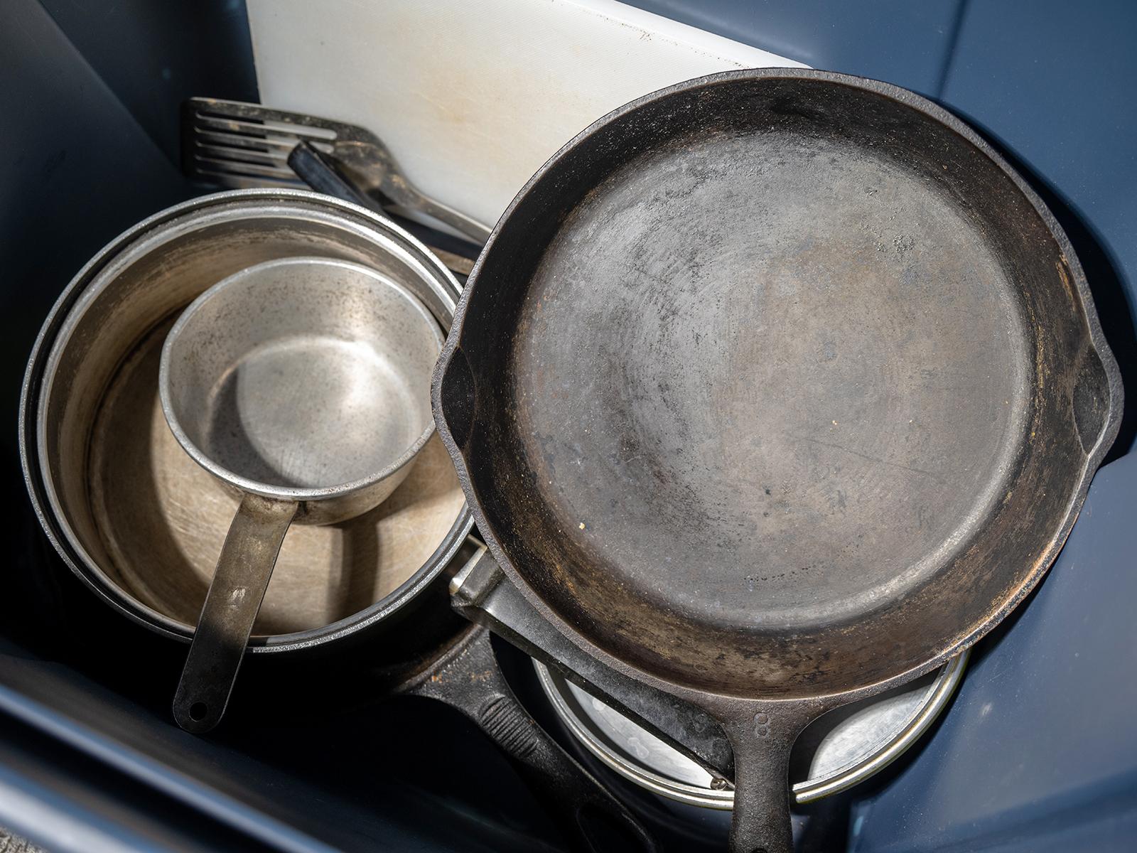 A close up photo of metal pots and pans for use. Stored inside a blue plastic tub.