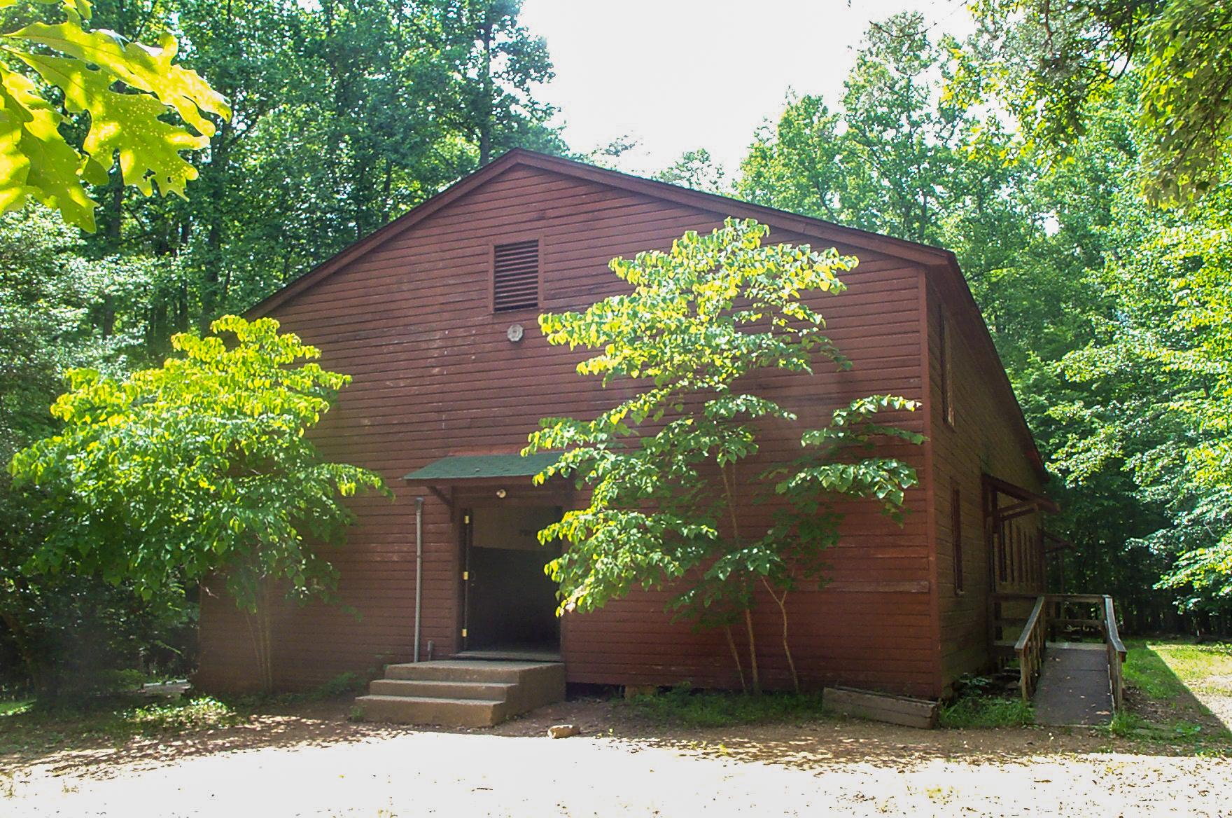 A reddish brown wood building with its front door open sits among trees