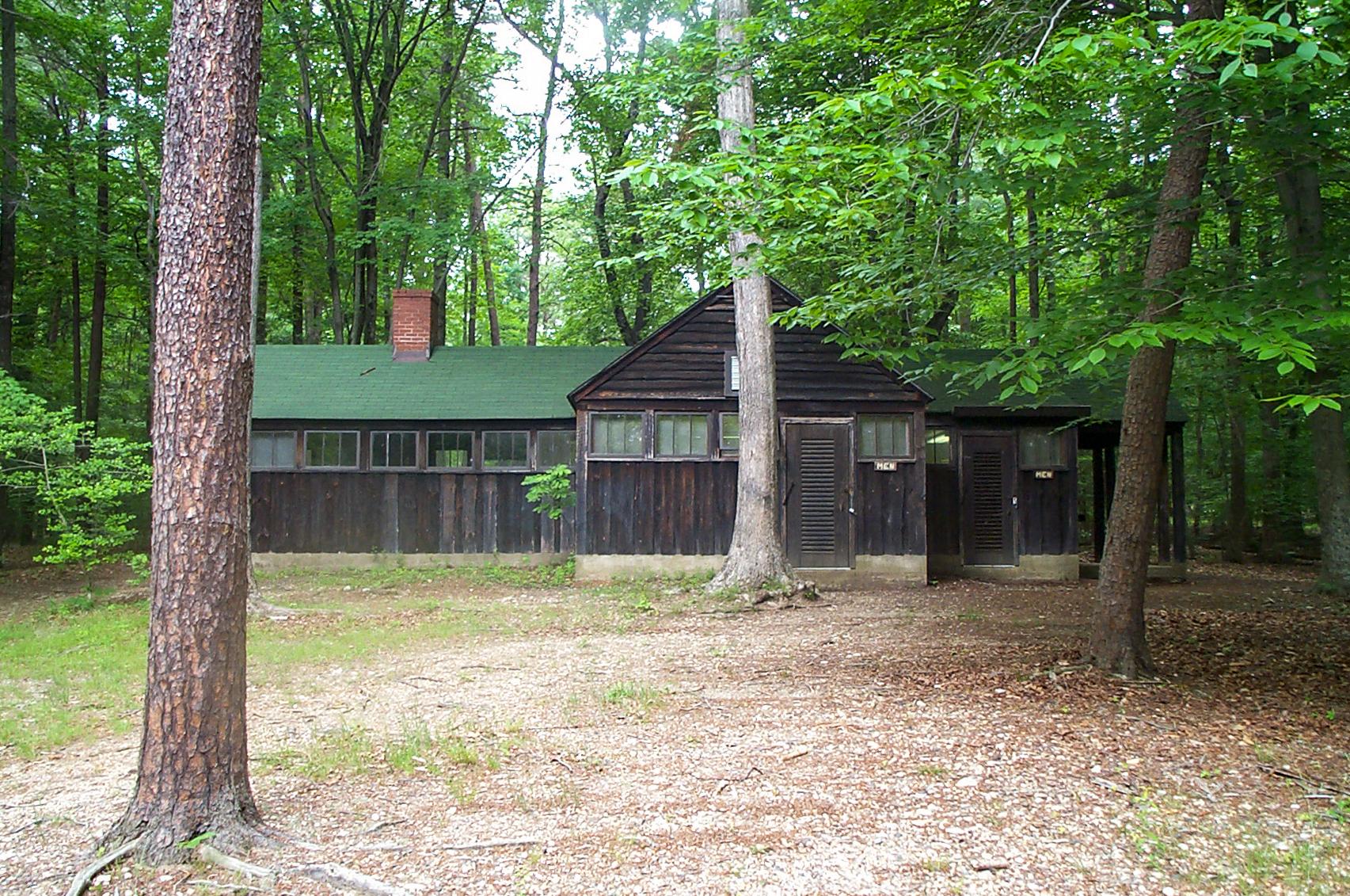 A dark brown wooden building with a green roof sits among trees