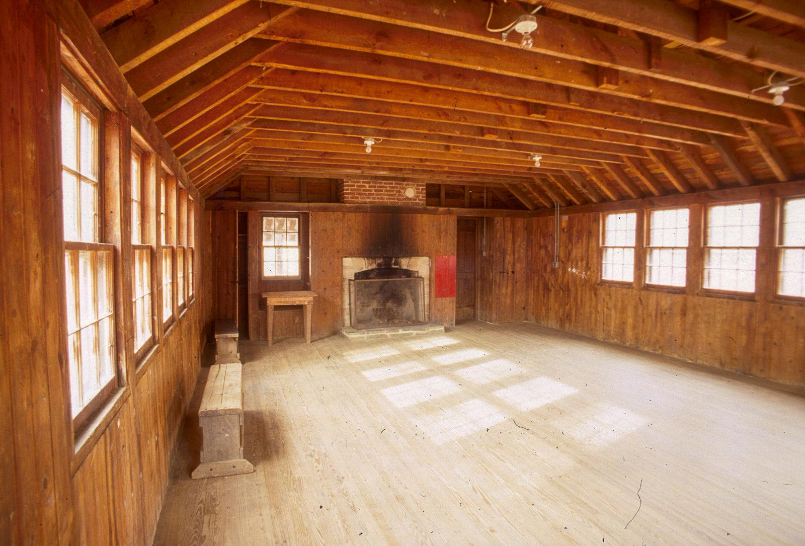A room with a wood floor and exposed wood rafters has a brick fireplace and benches around the edges