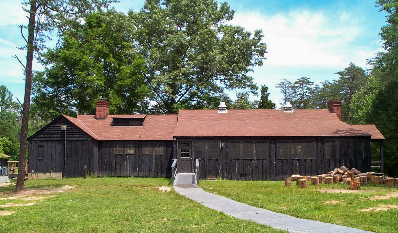 A dark brown building with an orange roof stands among trees and a grassy lawn.