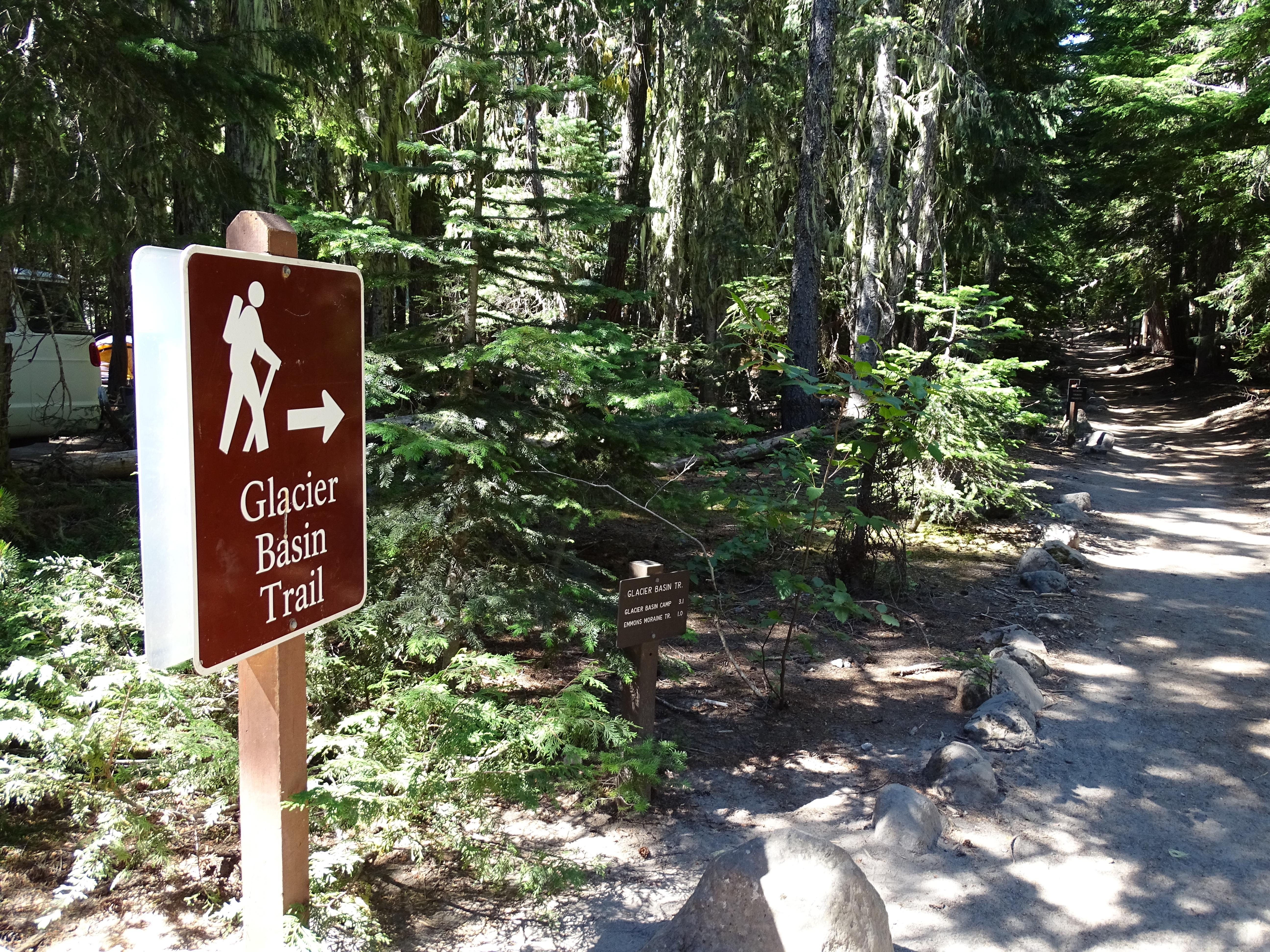 A brown sign pointing to a forested trail.
