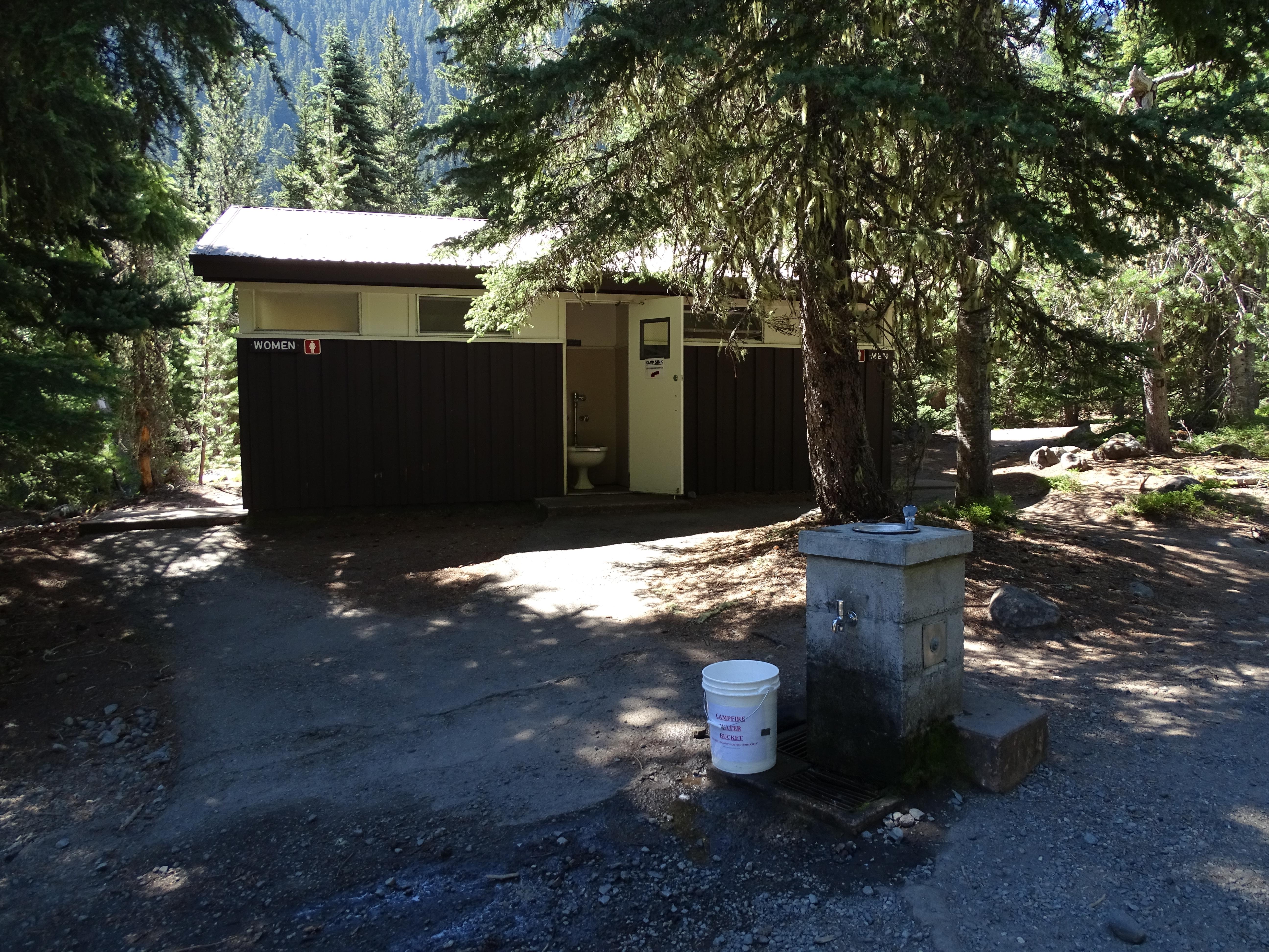 A brown bathroom building behind a small stone structure for getting water.