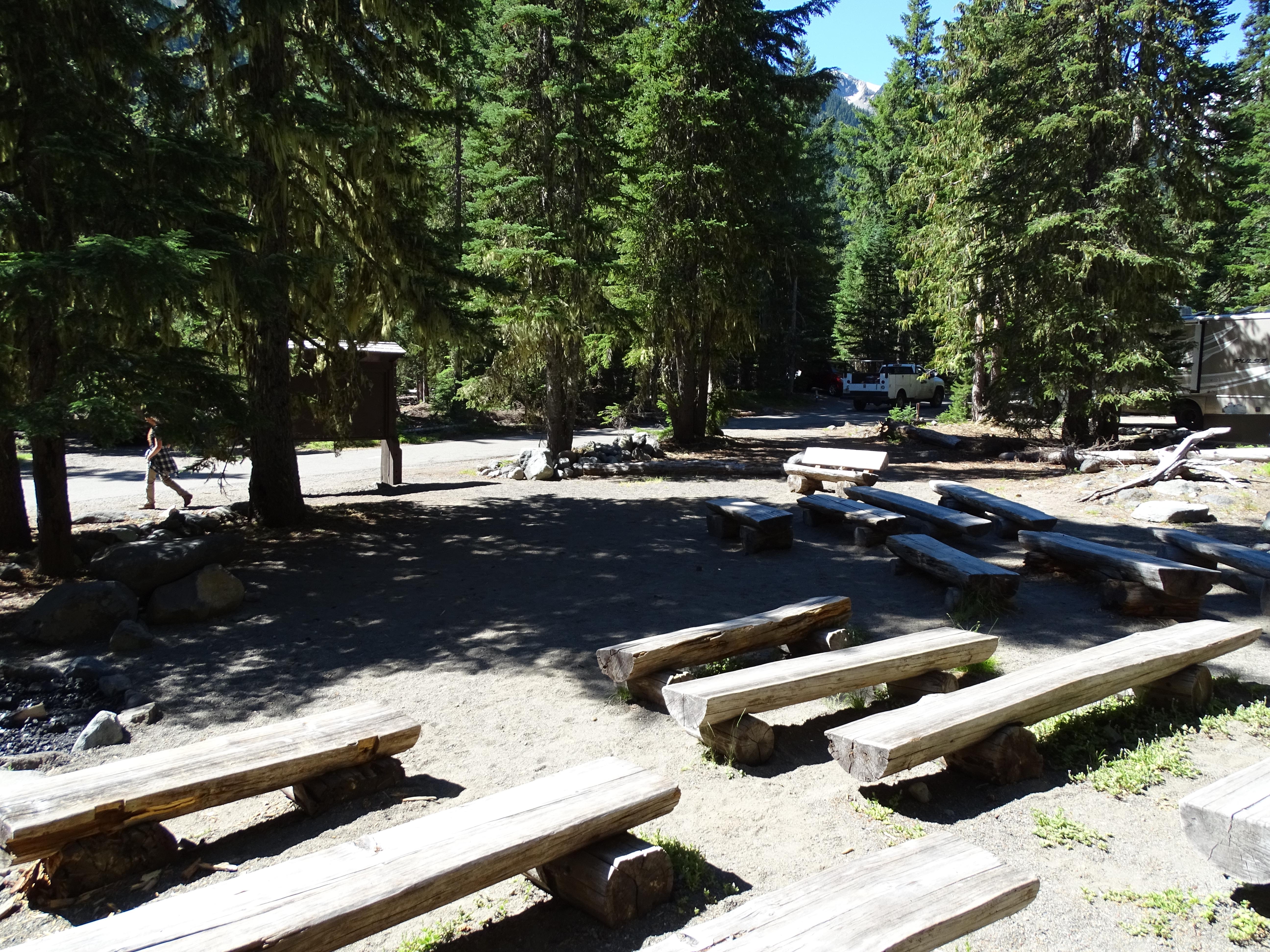 Rows of wooden benchs around a campfire circle.