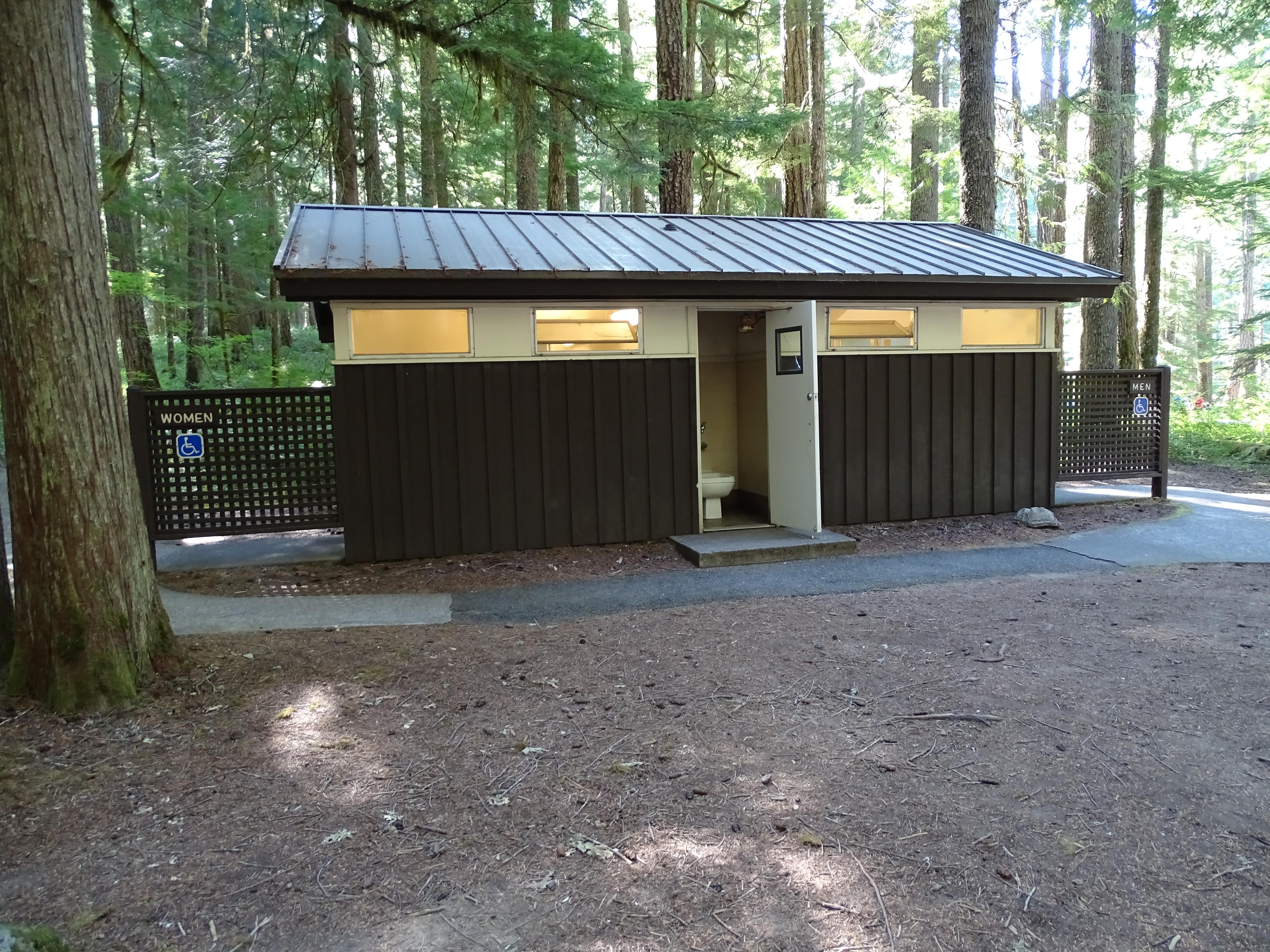 A brown bathroom building with forest behind.