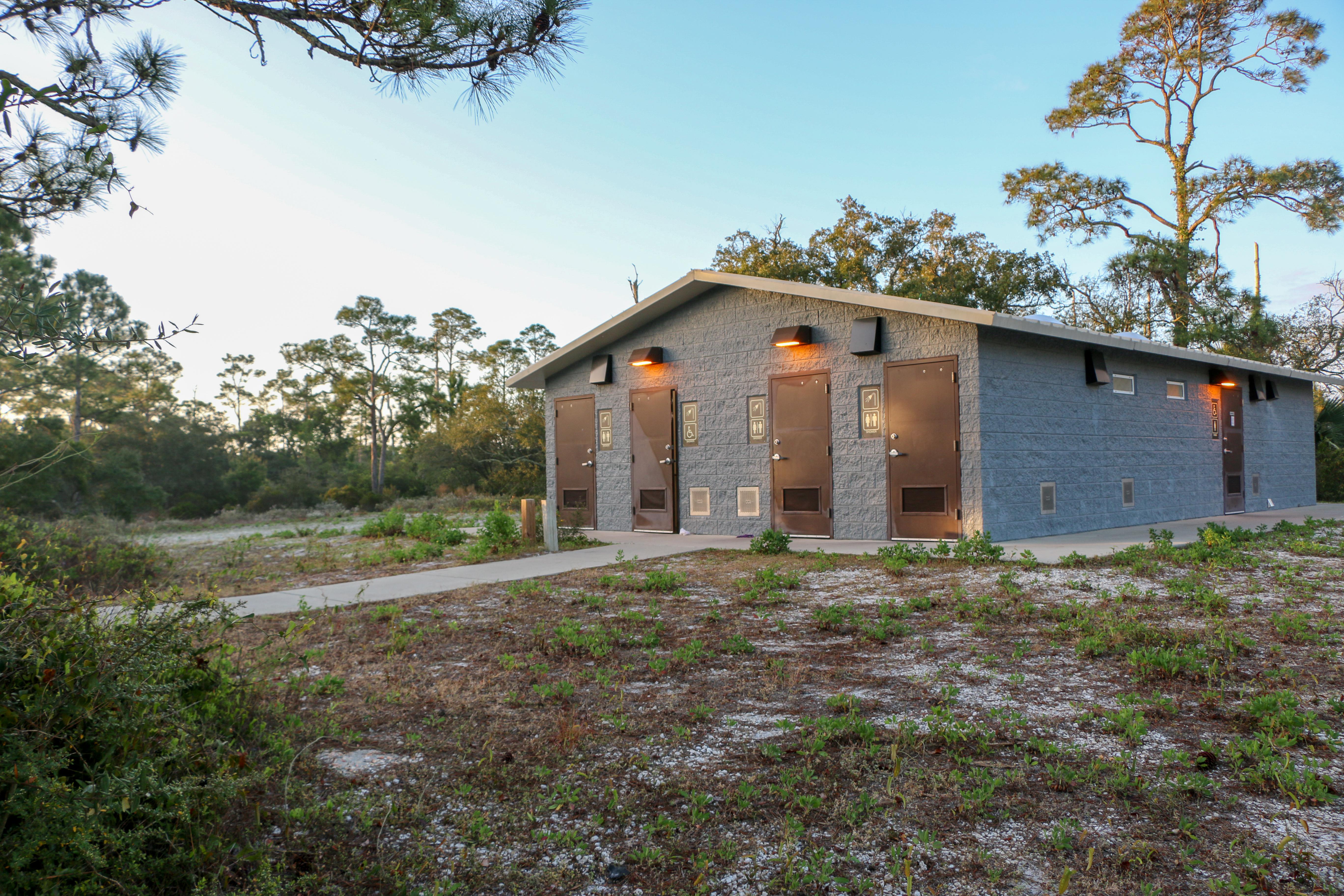 The sun reflects off of a concrete structure with four shower entrances.