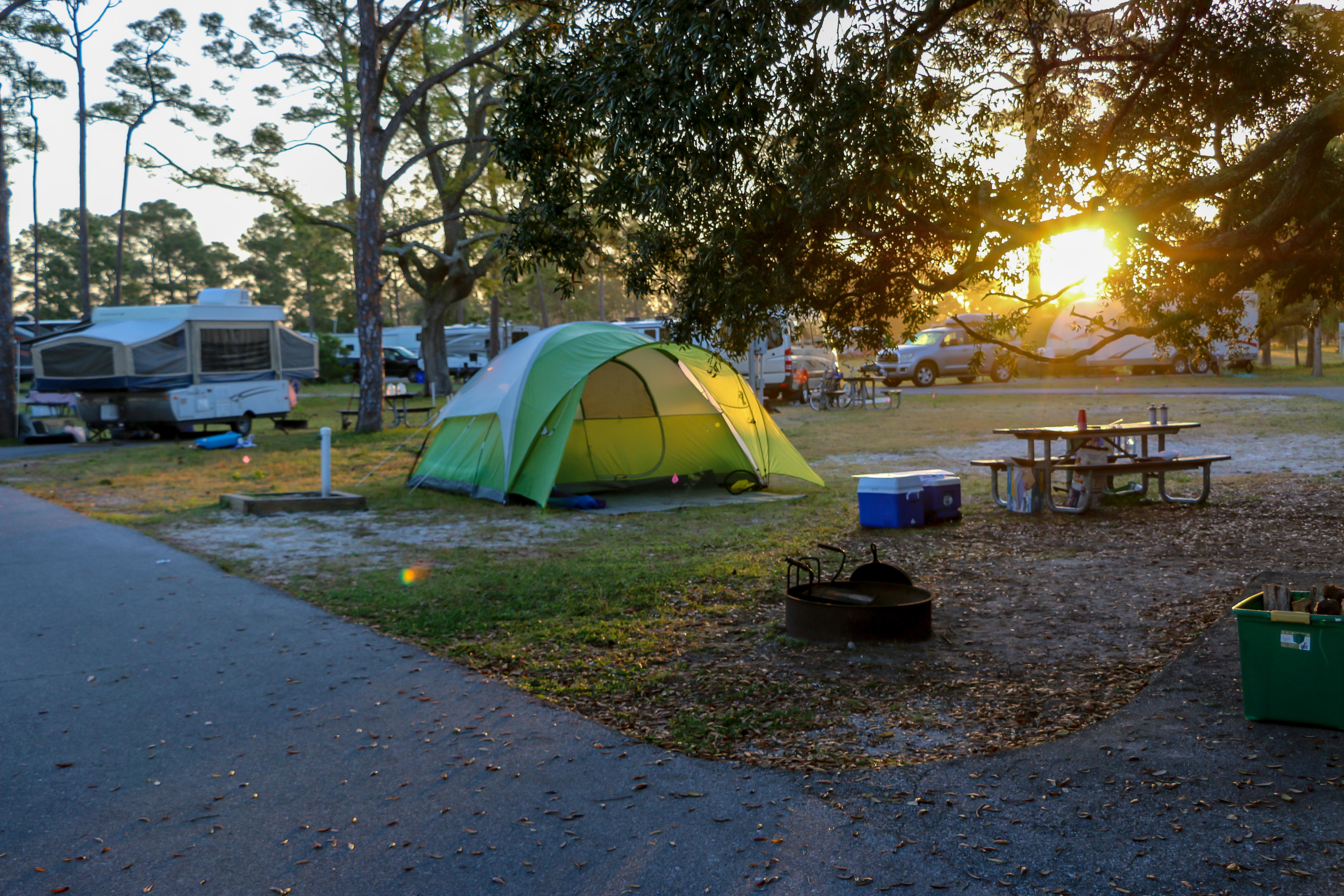 The sun sets on a small tent set up in the grass near a small road.