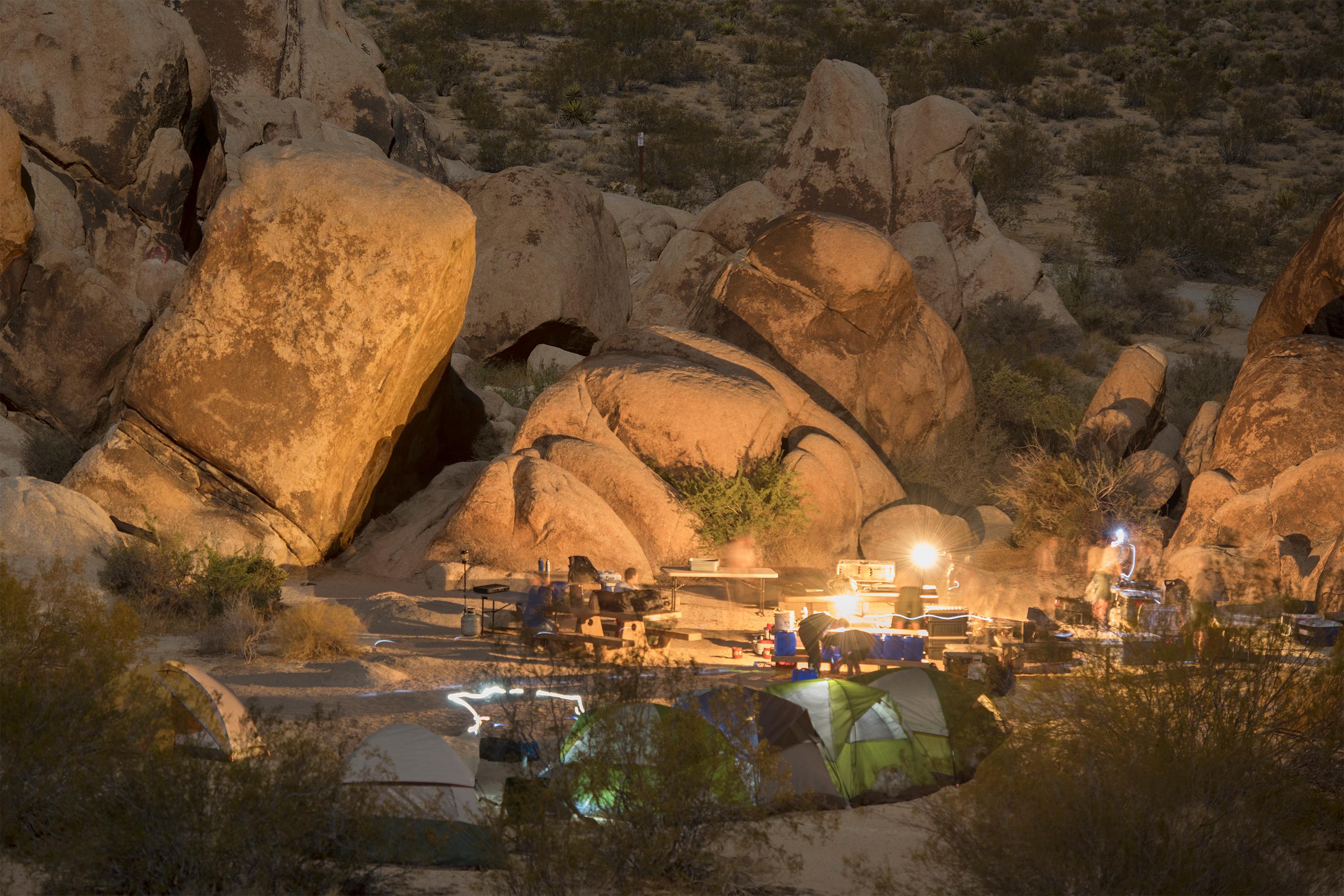 Several tents and picnic tables lit up in the evening in front of large rock formations.