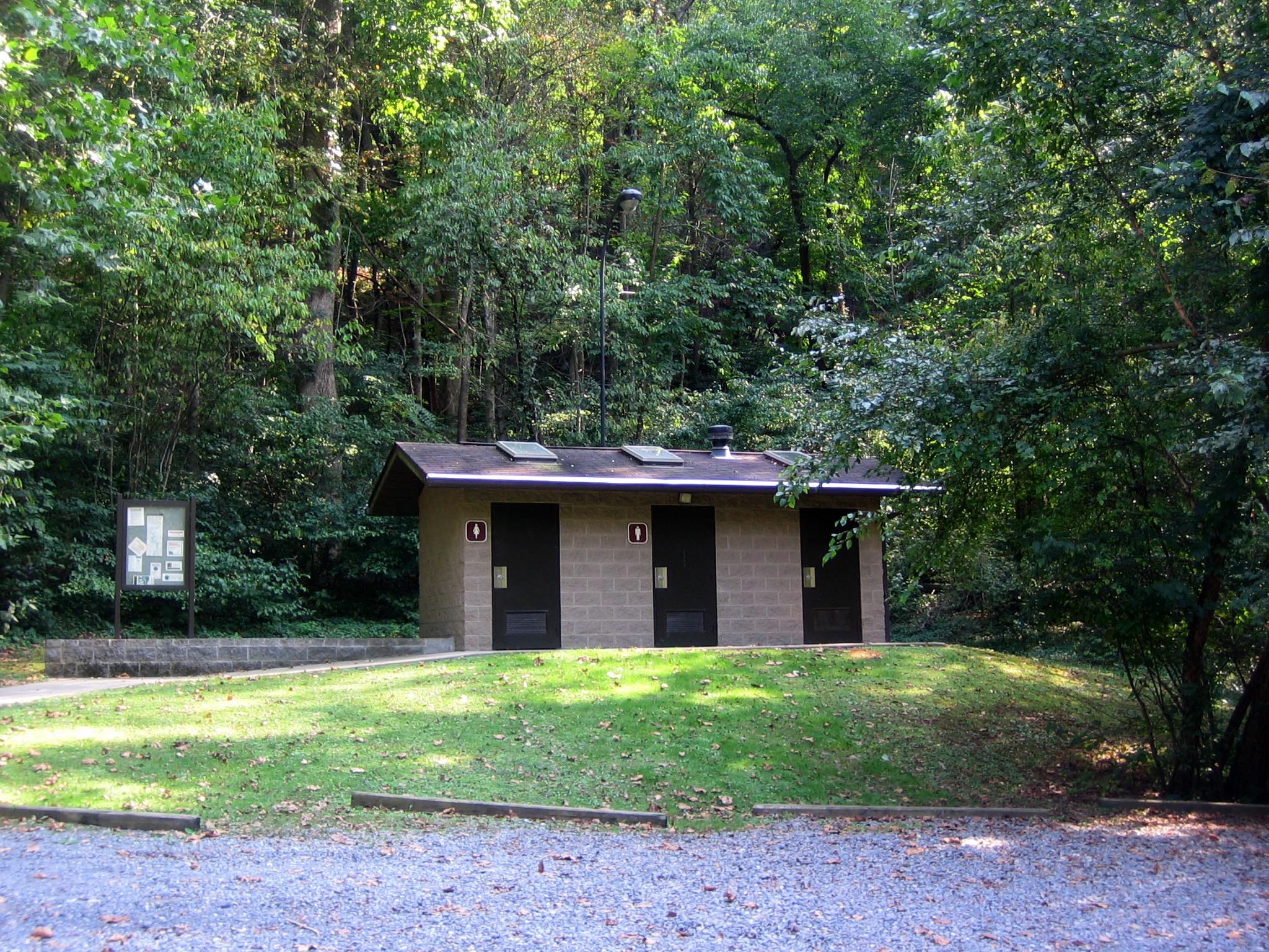 A tan building on a grassy hill with three brown doors marked as restroom facilities.