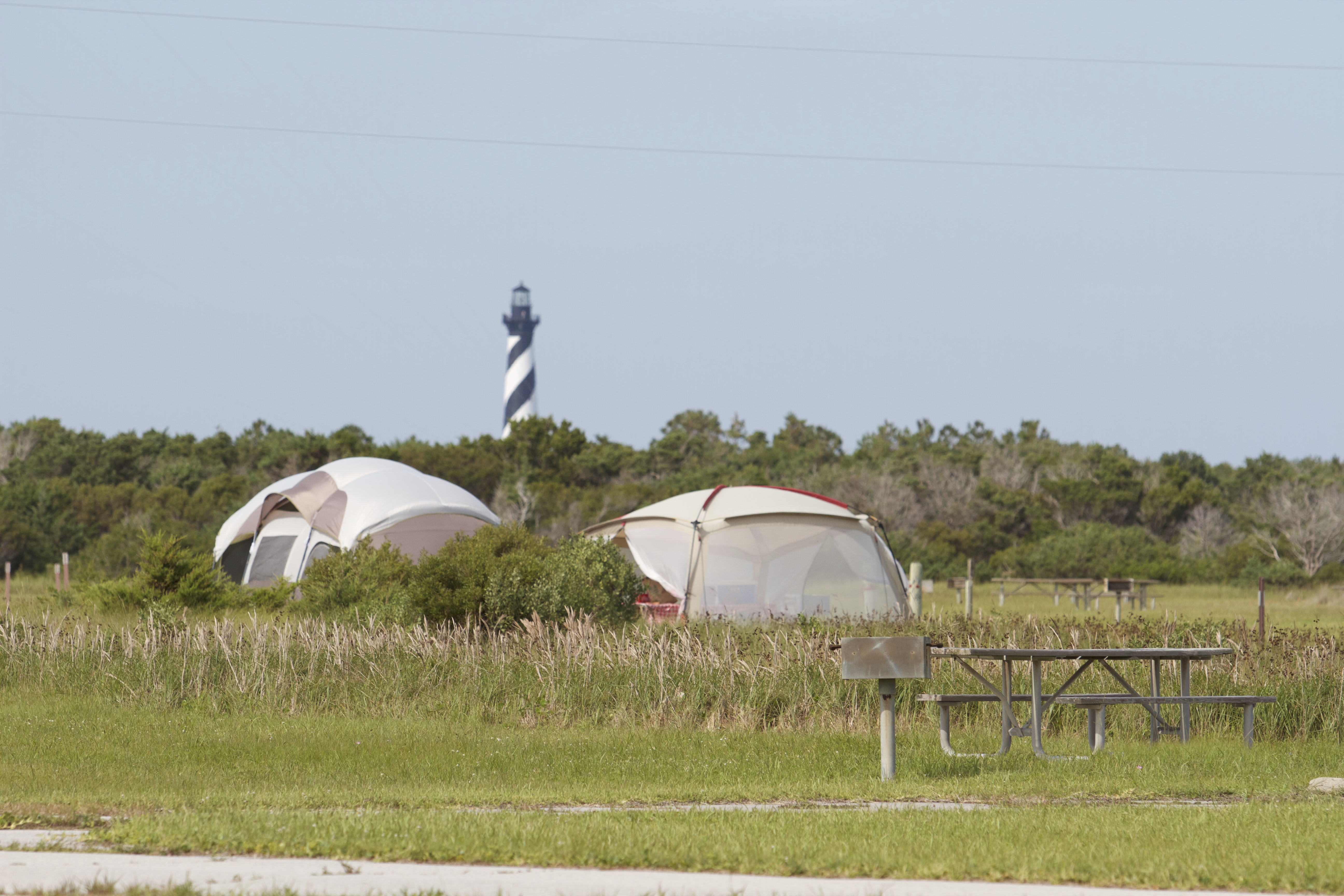 Two tents and the Cape Hatteras Lighthouse visible behind a grassy camp site.