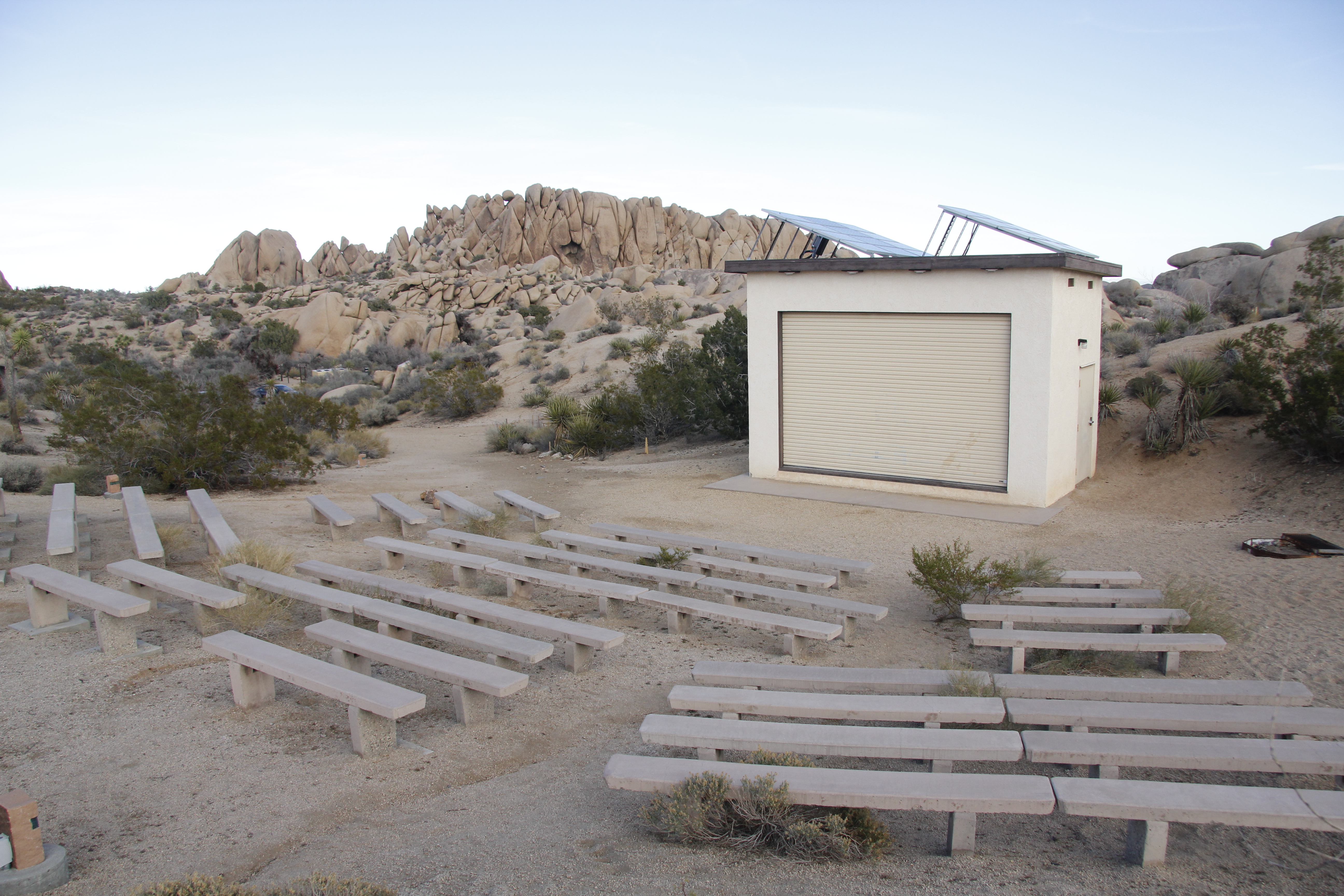 Rows of seats are in front of a stage. Behind the stage are large rock formations.