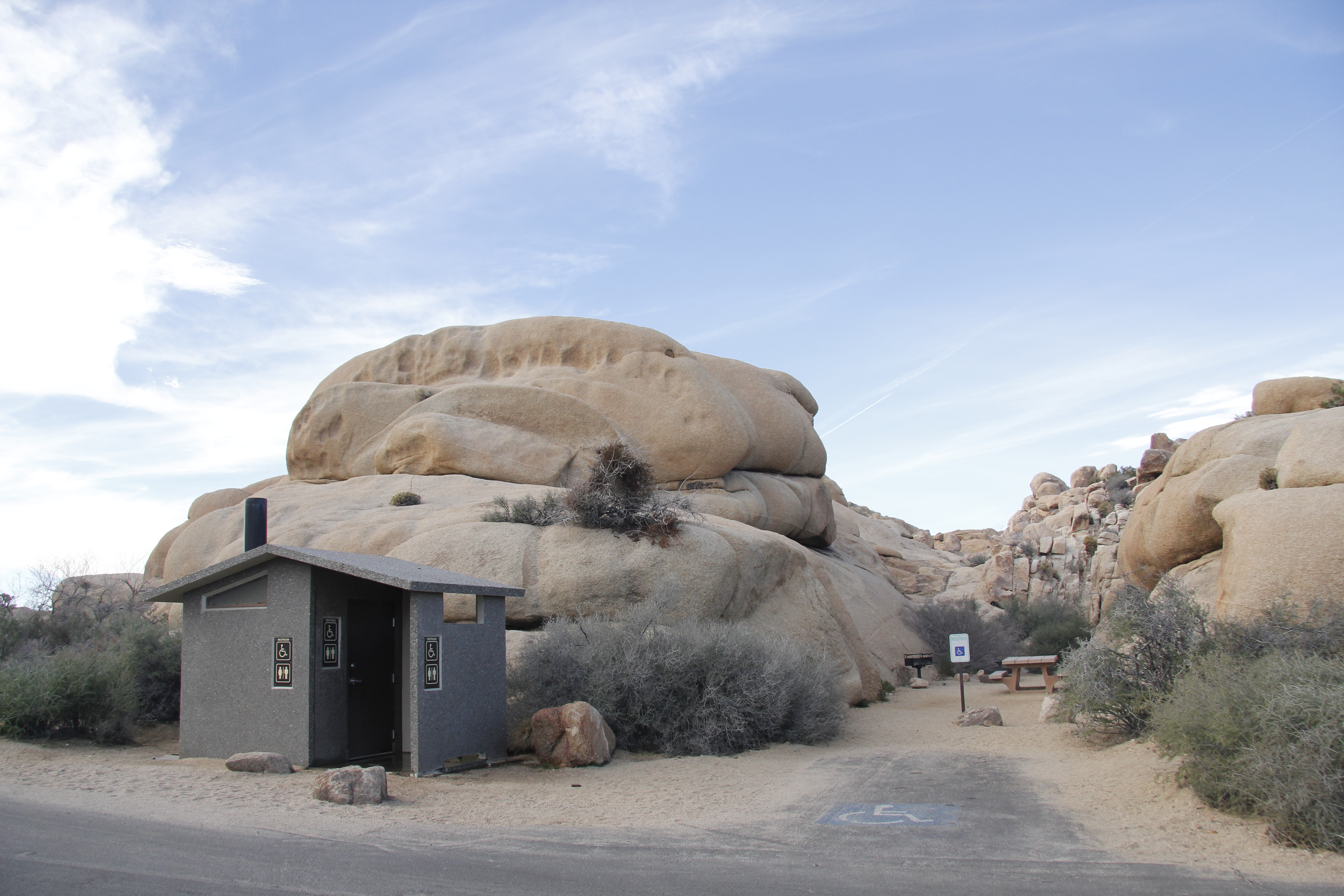 A campsite with a parking space in front is next to a restroom.