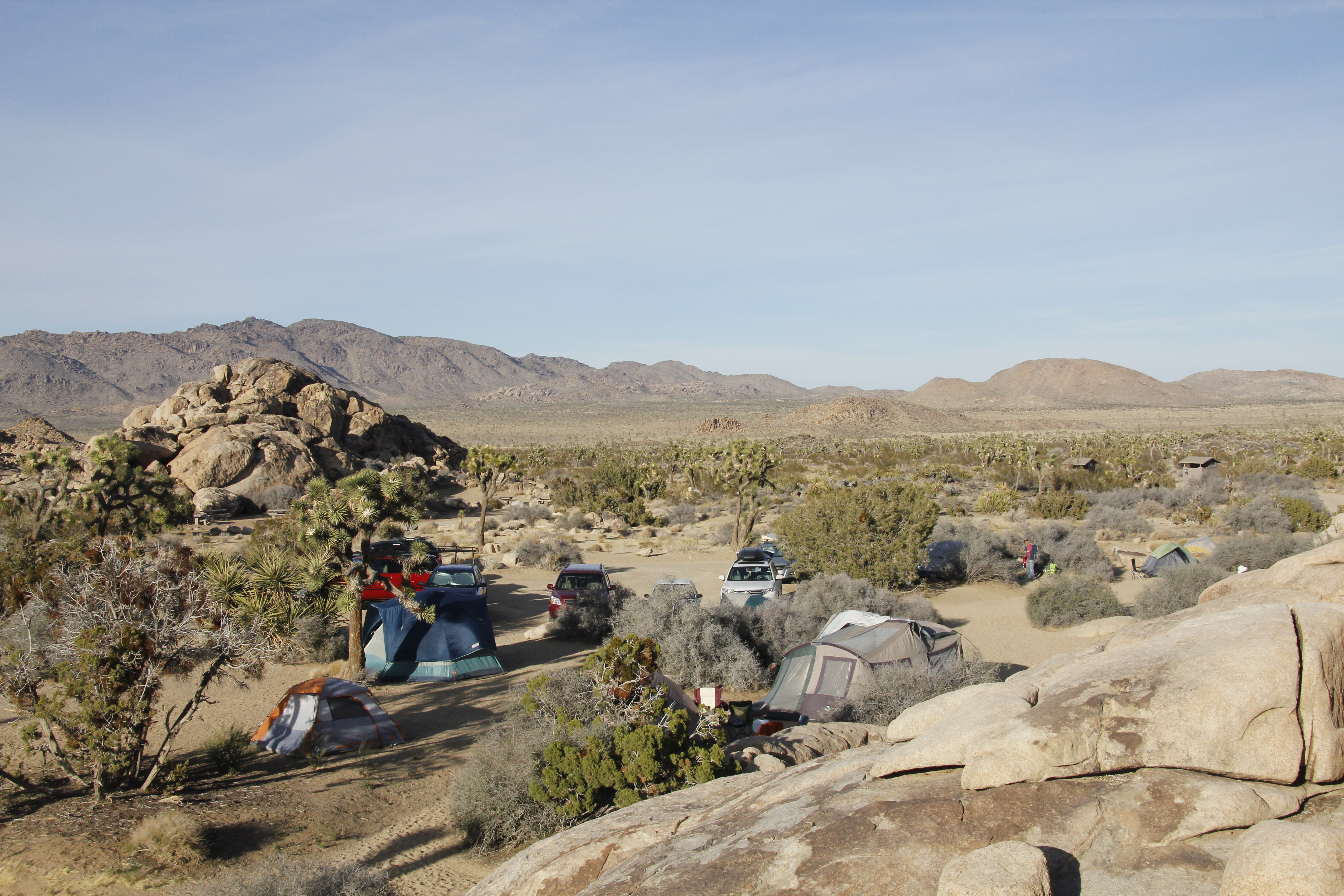 A landscape view of the campground with a campsite, tents, a parking lot, and a dirt road in view.