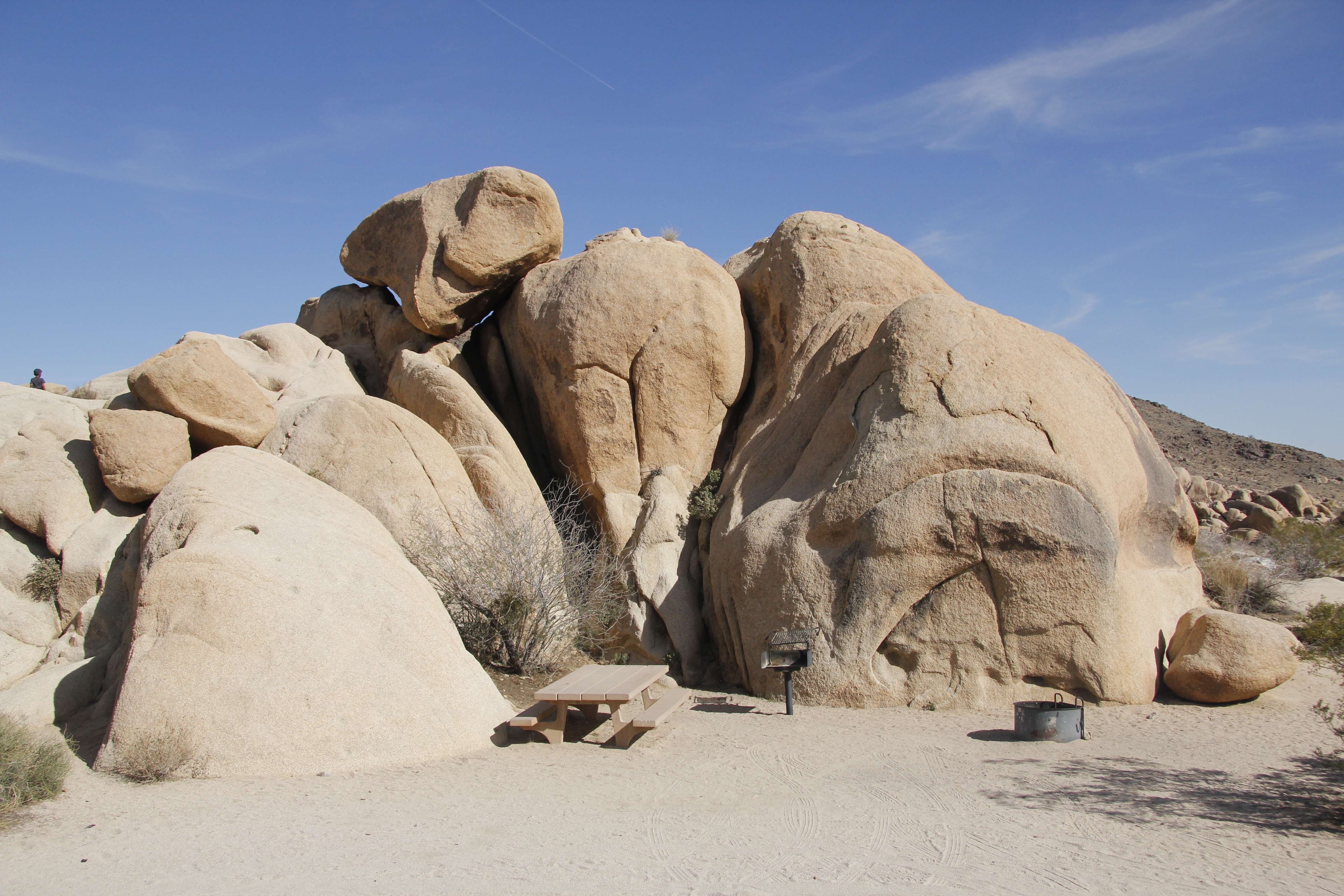 A picnic table and fire ring are in a campsite adjacent to a large boulder.