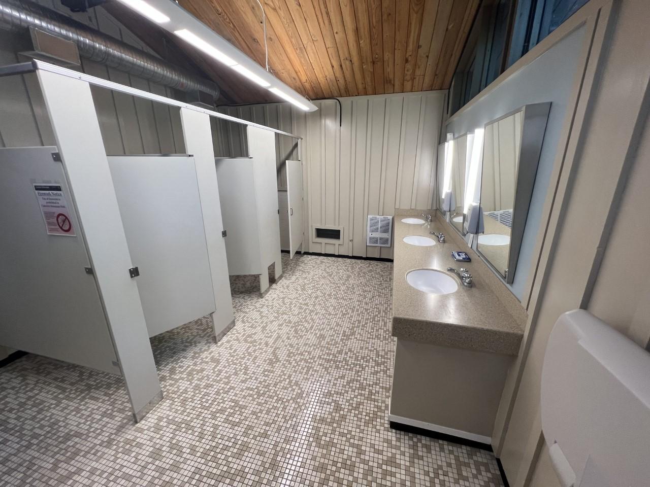 Interior of a restroom with three stalls and sinks. It is clean and well lit.