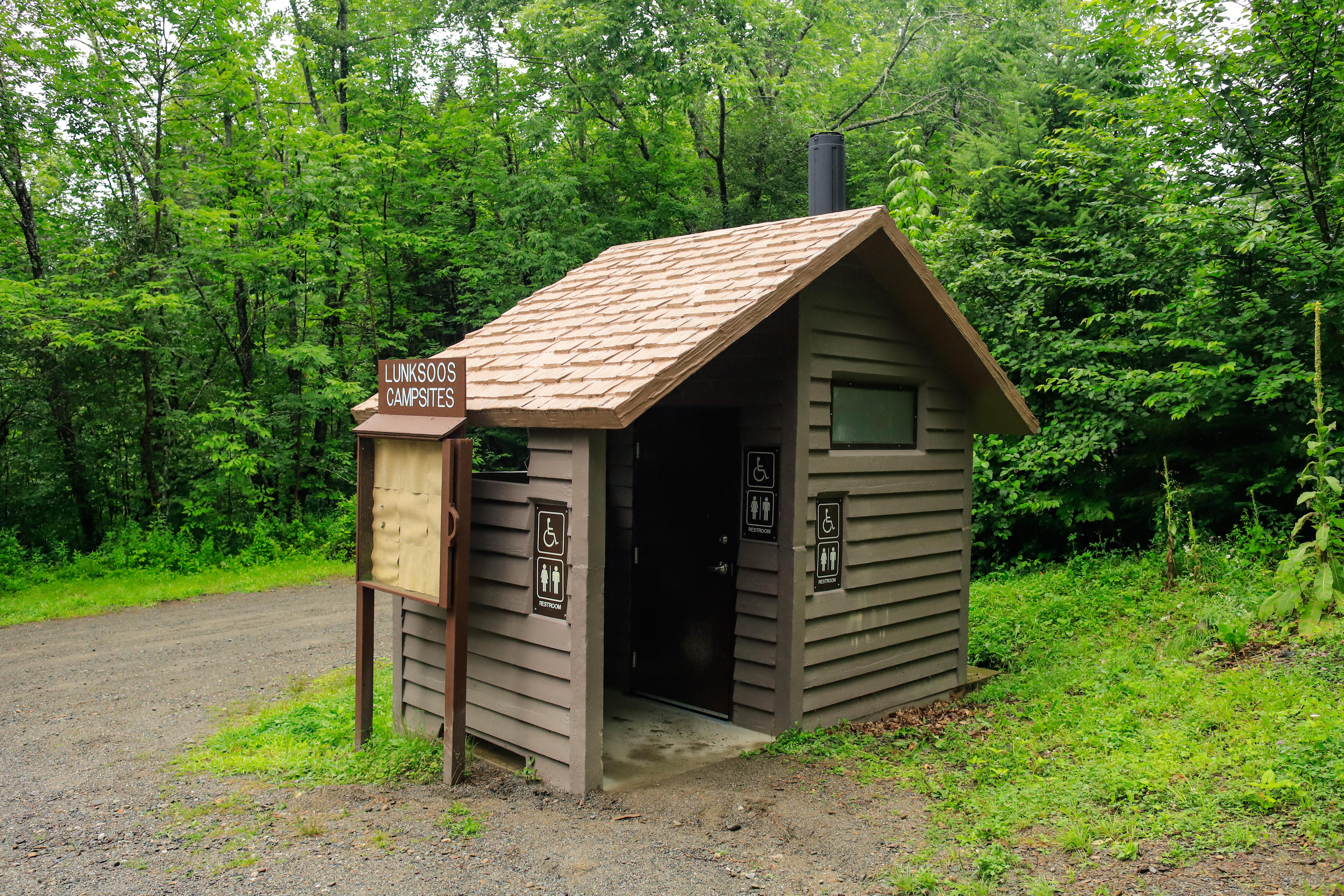 A vault toilet facility with a campsite sign reading "Lunksoos Campsite" and poster board