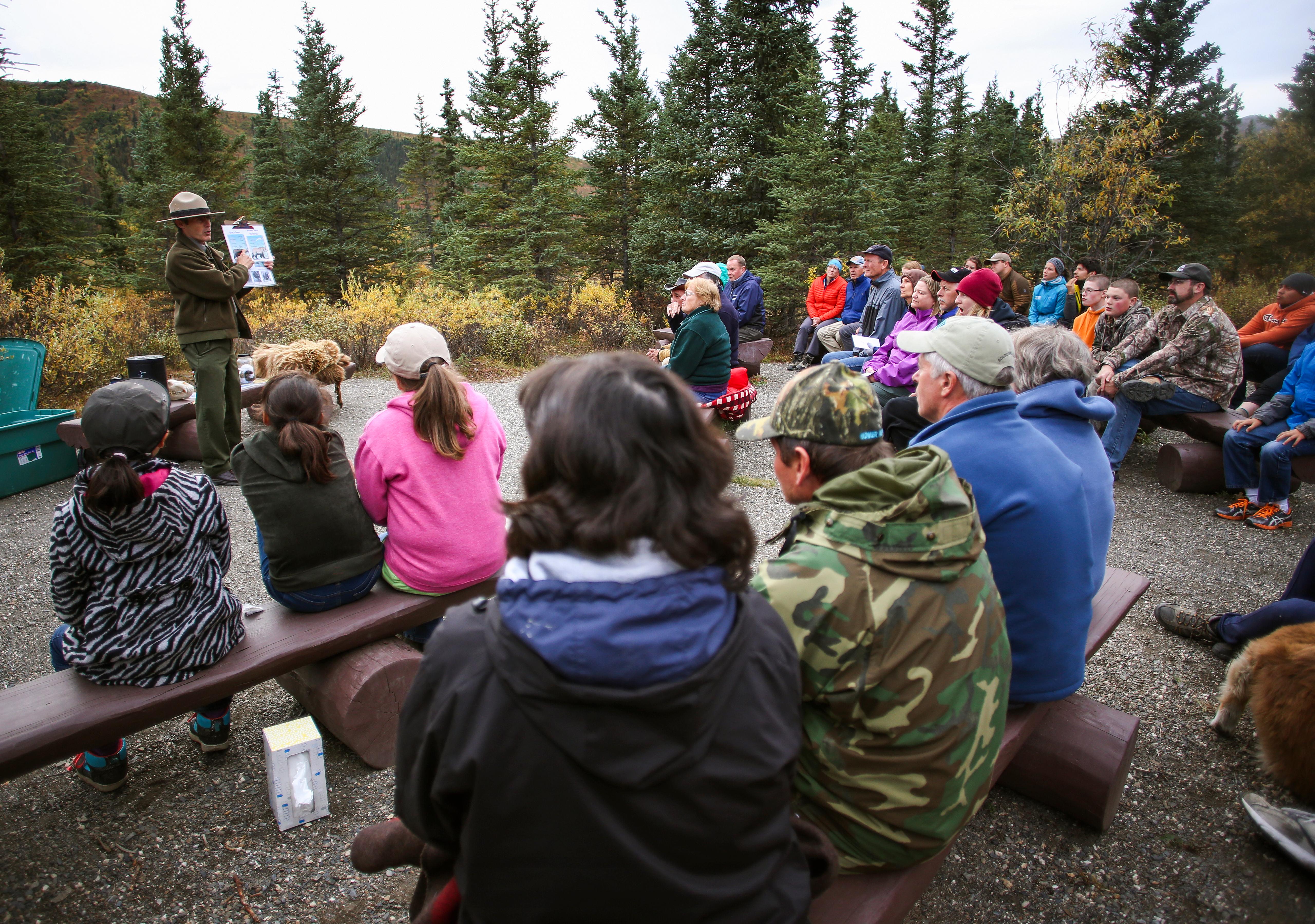a crowd sitting on benches faces a park ranger giving a talk