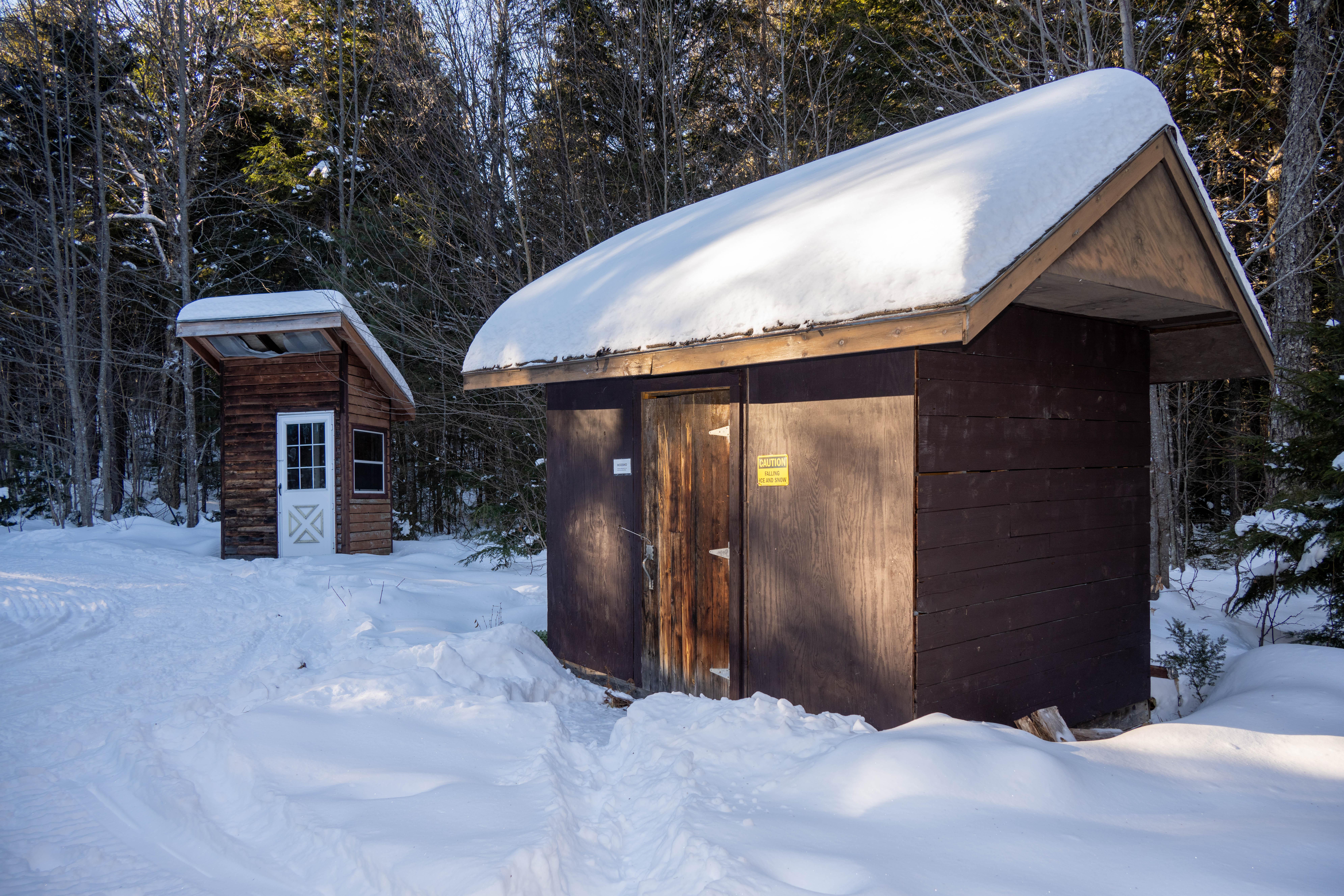 A small wooden shed with a tick layer of snow on the angled roof. Thick snow is on the ground.