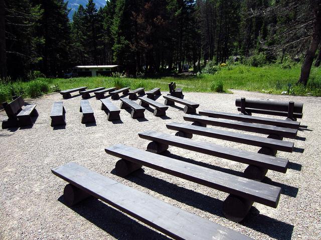 wooden benches on gravel clearing with campsites and bathroom building in background among trees