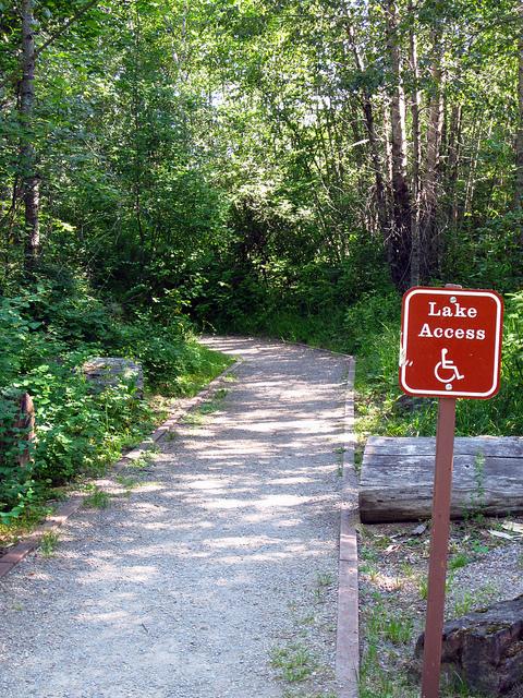hard packed trail in woods marked with accessible symbol on sign