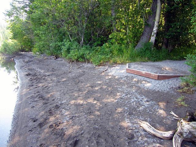 hardpacked gravel pad at forest edge, dark sandy beach at shoreline