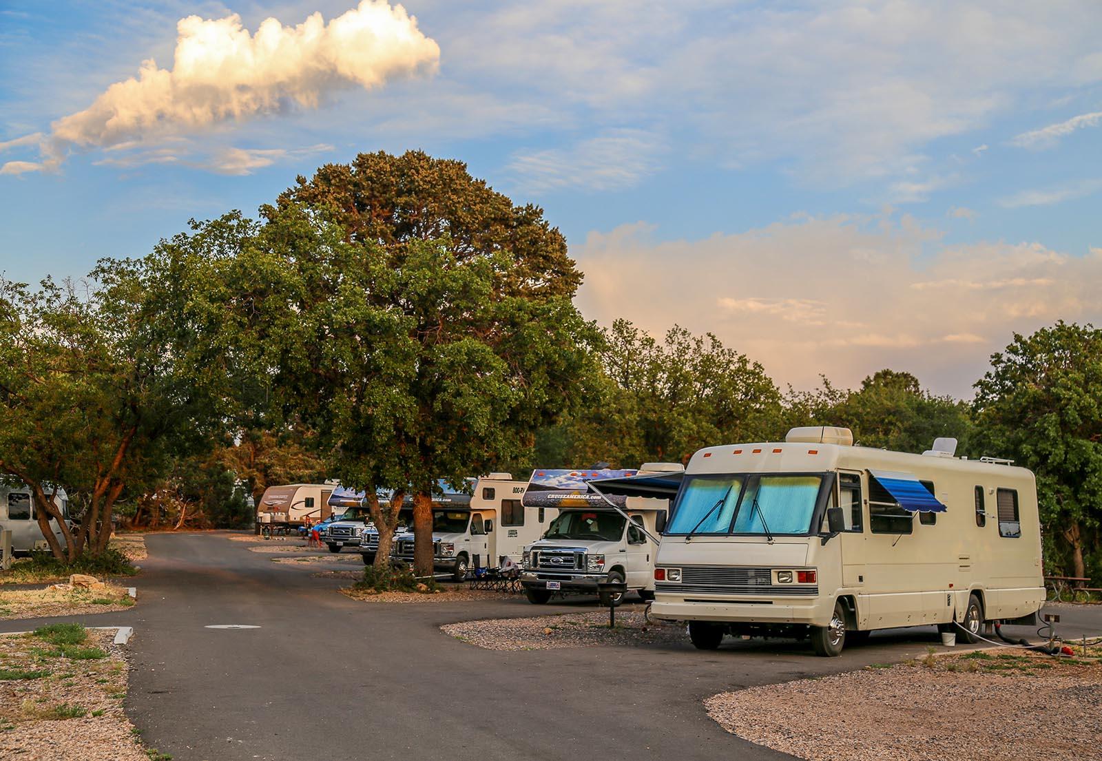 A road with 5 RVs and a trailer facing forward in individual pull-through sites